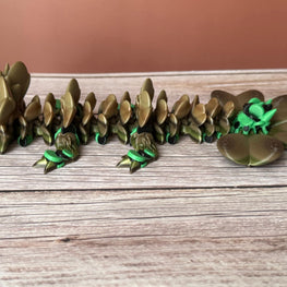 Brown and green 3D printed dragon figure with a clover shaped tail, placed on a wooden surface