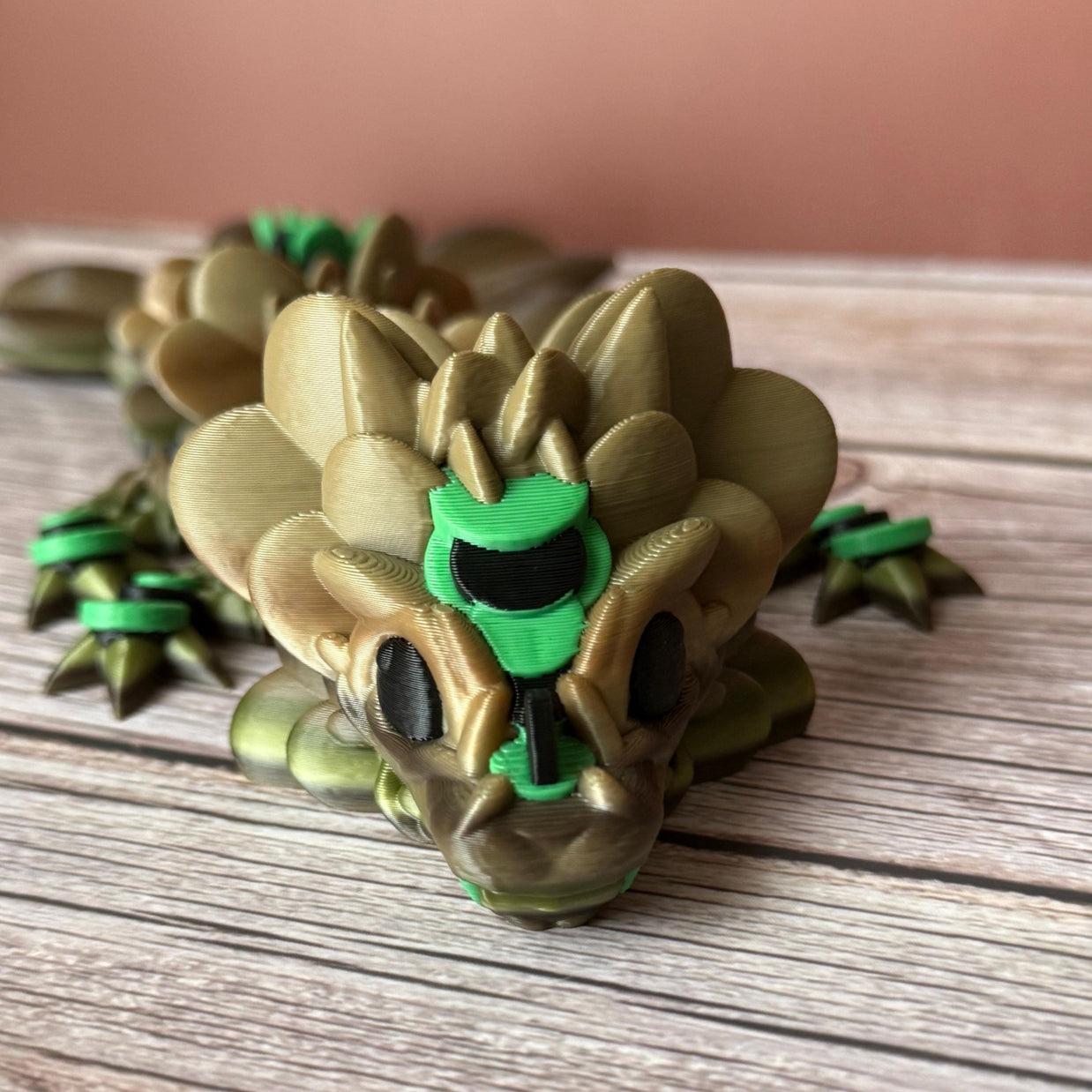 Brown and green 3D printed dragon figure with a clover shaped tail, placed on a wooden surface