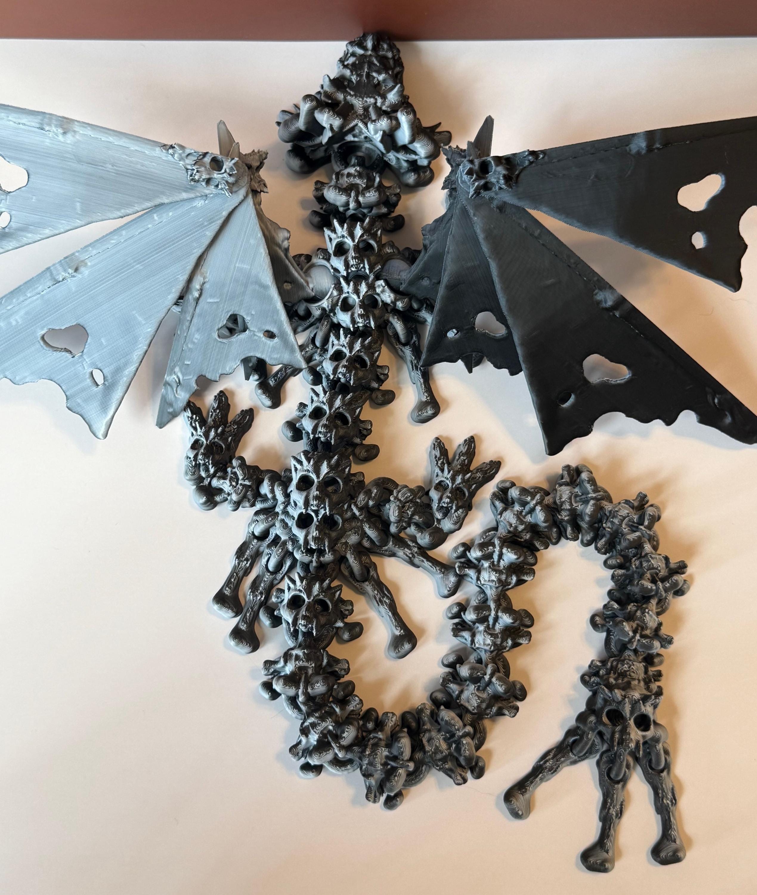 Winged black and white 3d printed dragon with a hollow theme consisting of skulls and bone-like features against a white and brown background