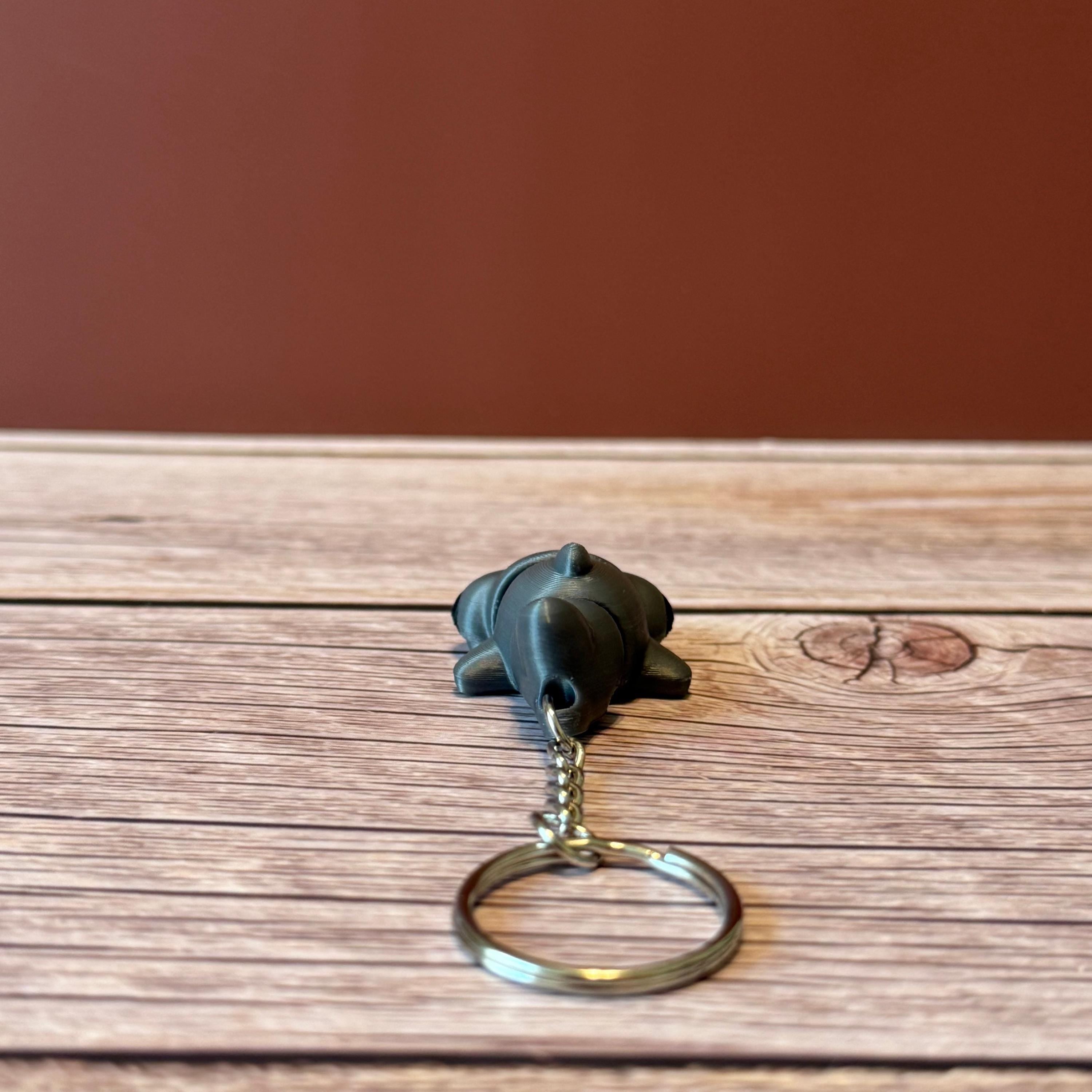 A 3D printed articulated hammerhead shark keychain in gray, displayed on a wooden surface.