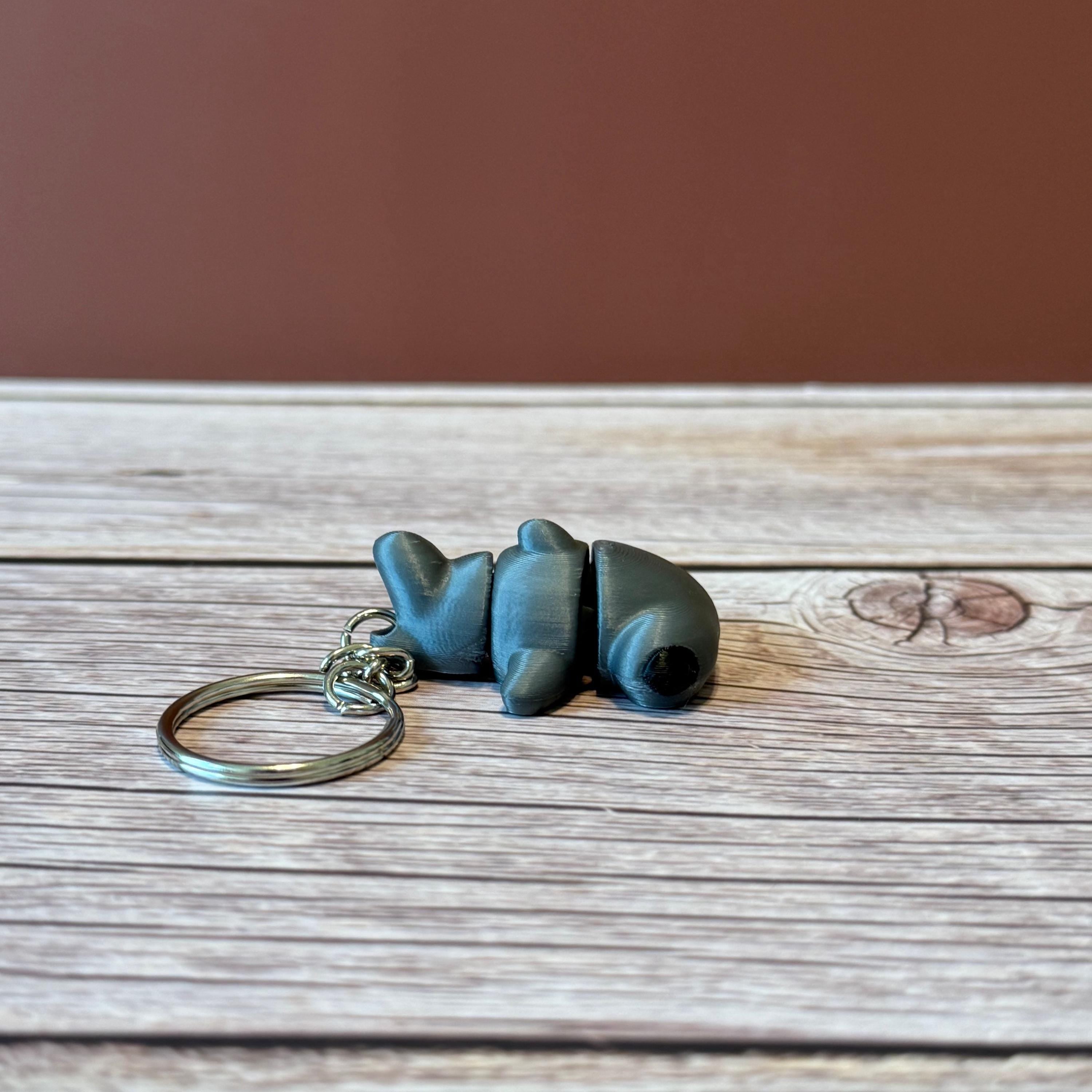 A 3D printed articulated hammerhead shark keychain in gray, displayed on a wooden surface.