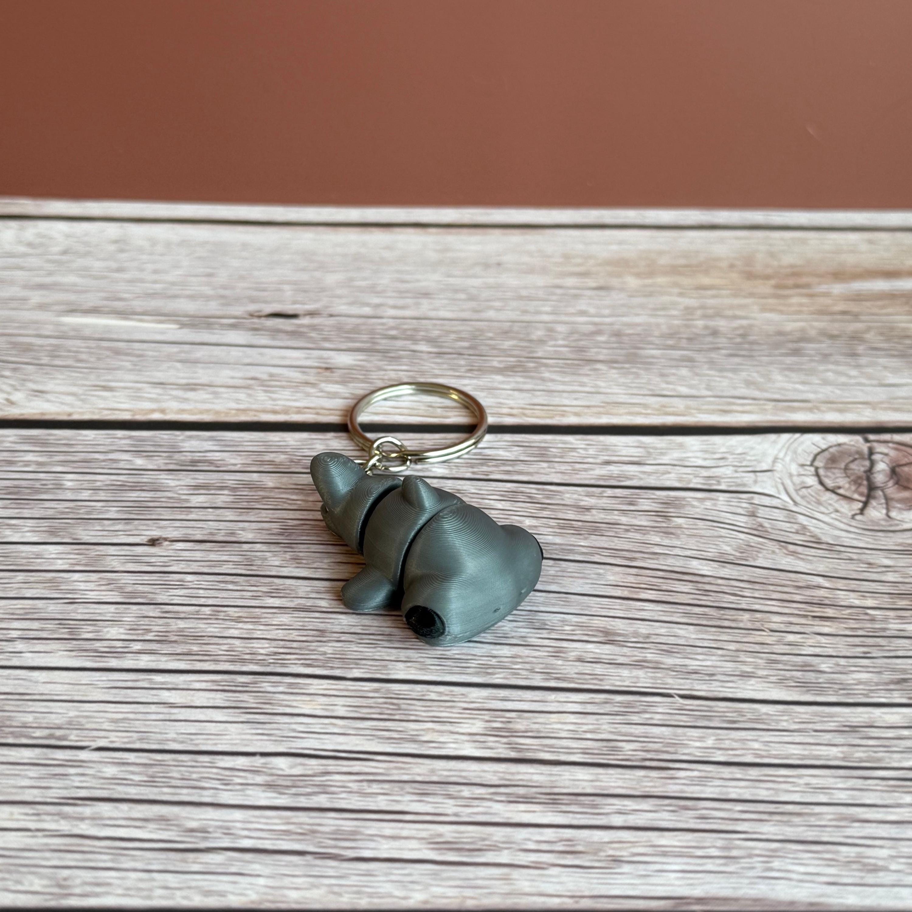 A 3D printed articulated hammerhead shark keychain in gray, displayed on a wooden surface.