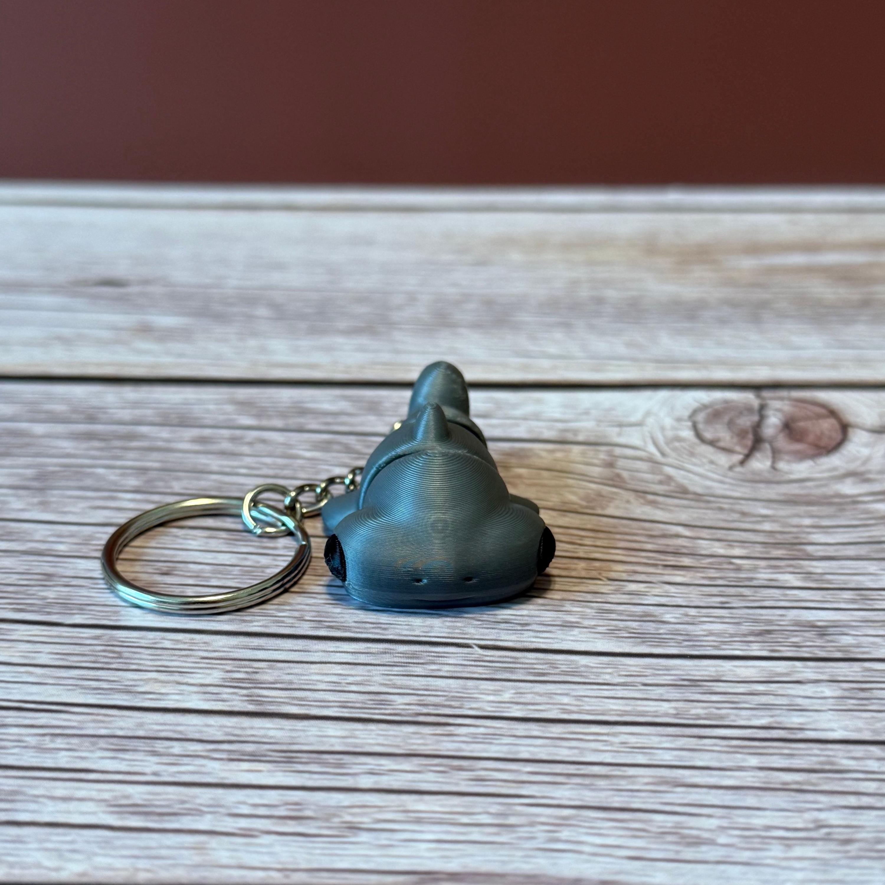 A 3D printed articulated hammerhead shark keychain in gray, displayed on a wooden surface.