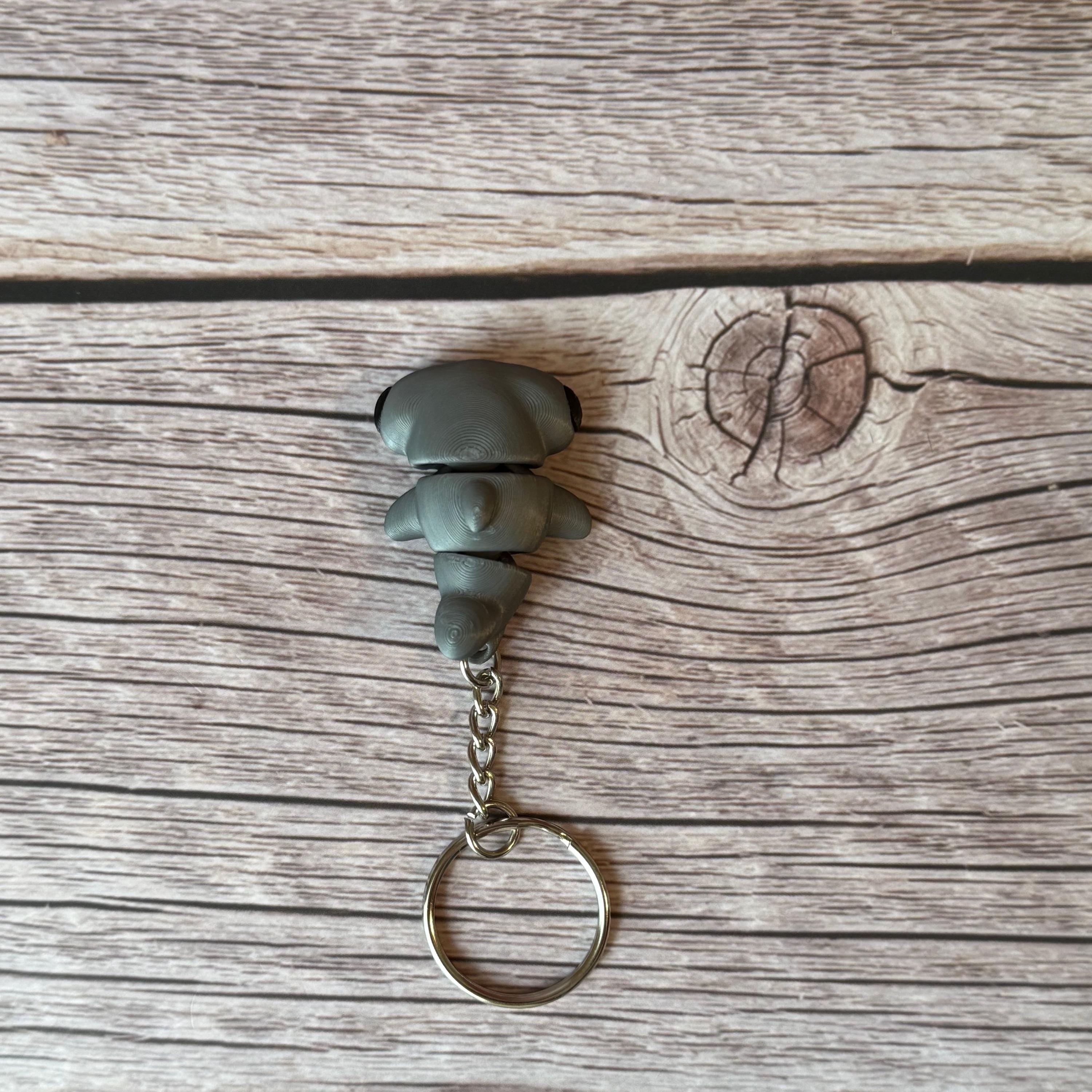 A 3D printed articulated hammerhead shark keychain in gray, displayed on a wooden surface.