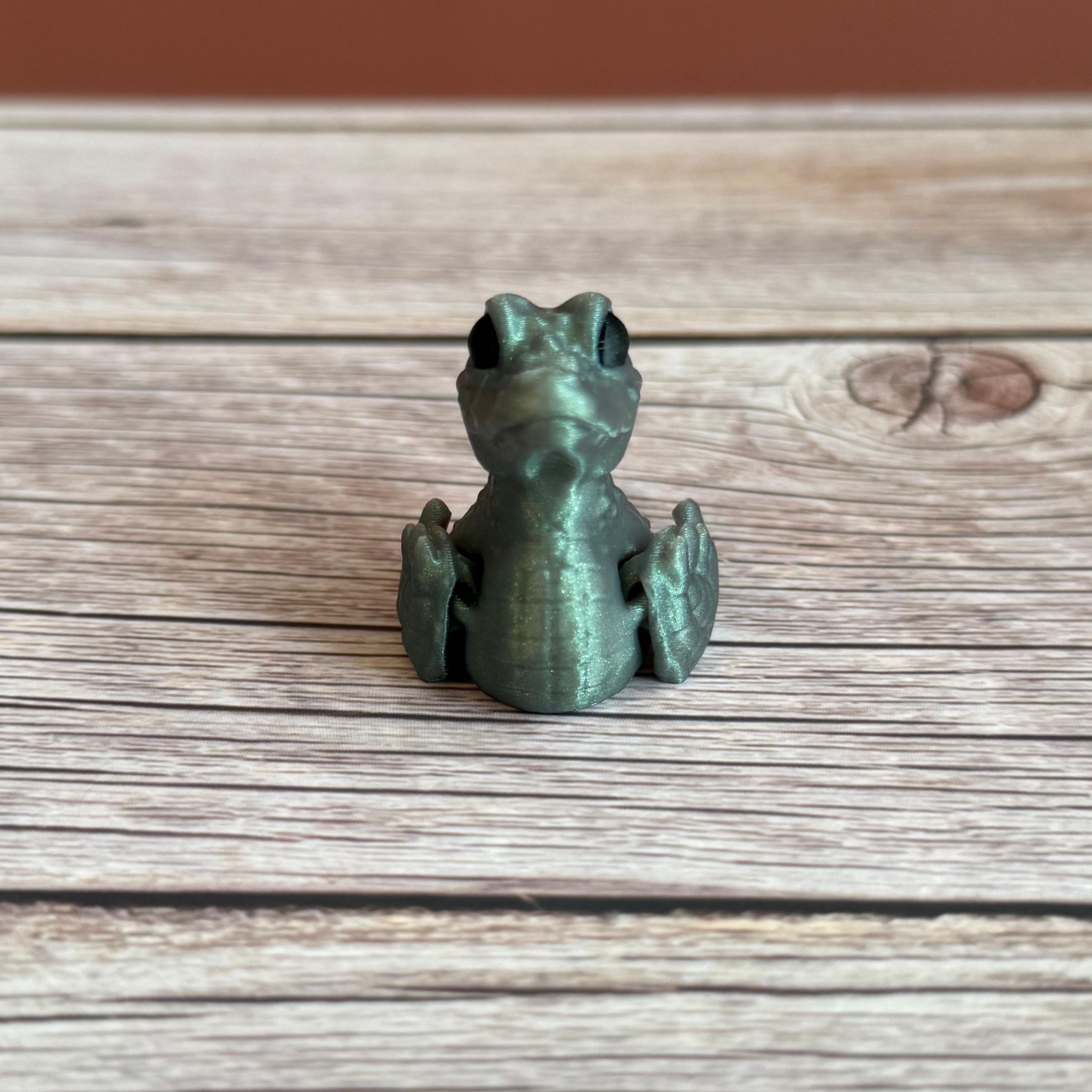 A small 3D printed figure depicting a hybrid animal resembling a duck and a crocodile, with a greenish tint, placed on a wooden surface.