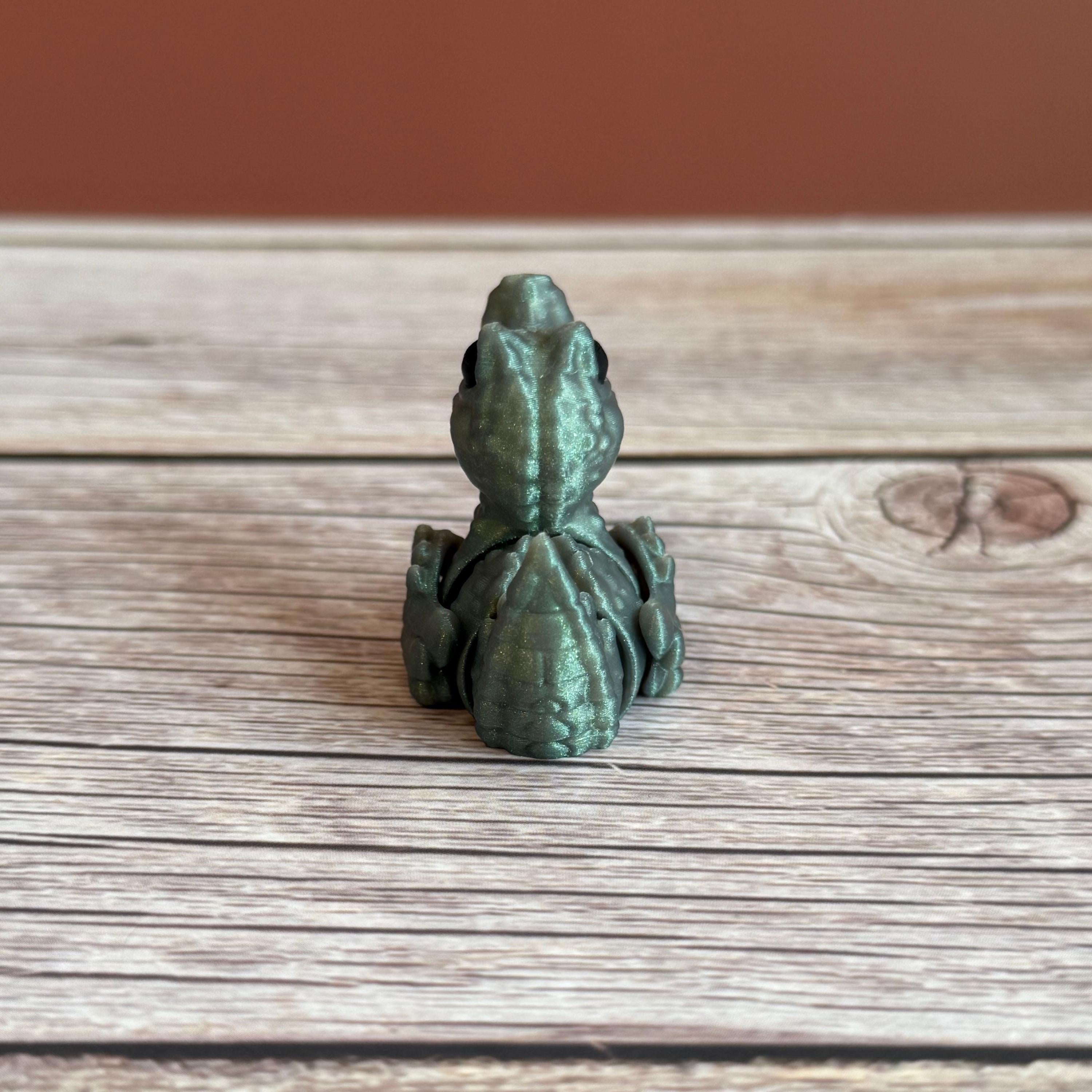 A small 3D printed figure depicting a hybrid animal resembling a duck and a crocodile, with a greenish tint, placed on a wooden surface.