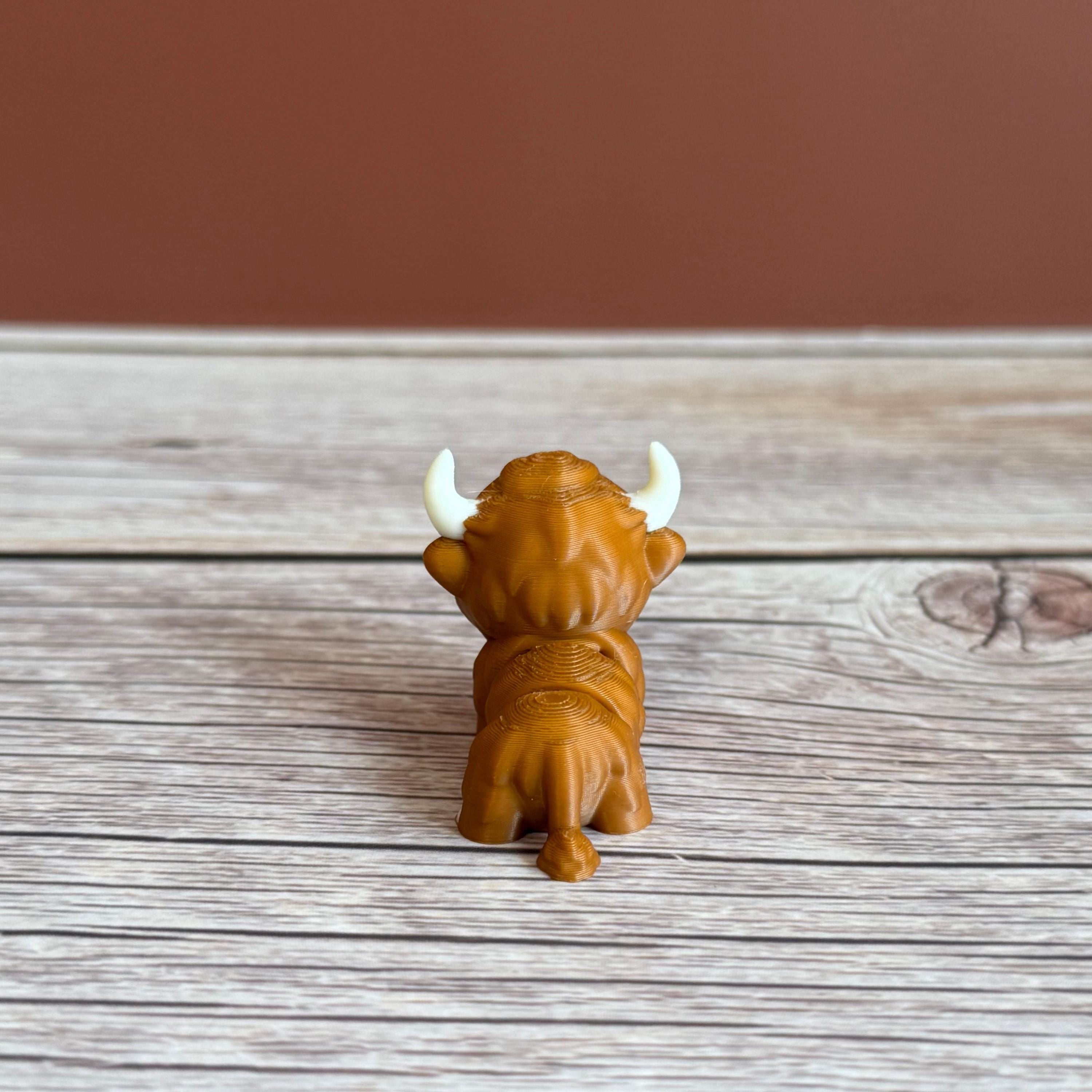 A small 3D printed articulated brown Highland cow toy with movable joints, placed on a wooden surface.