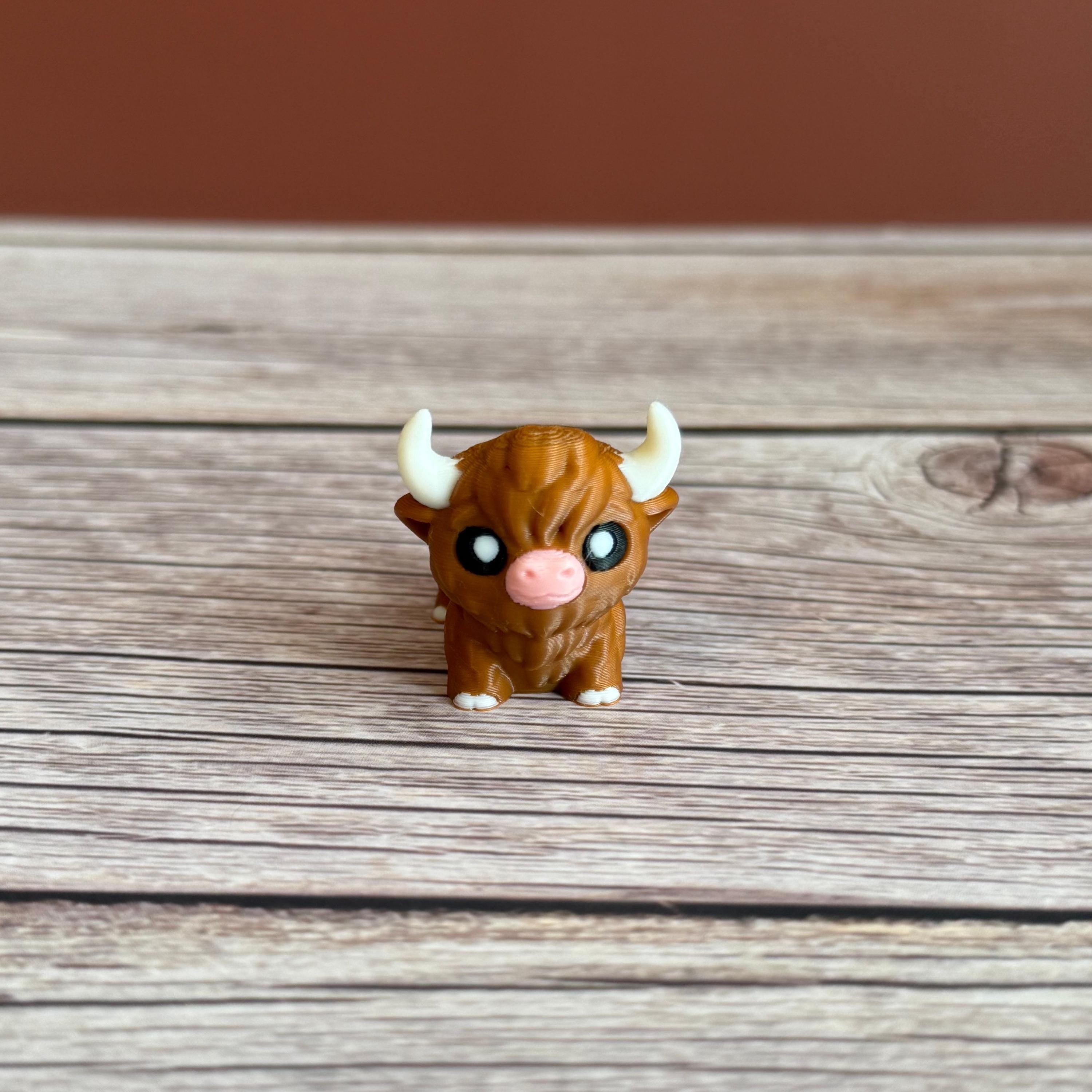 A small 3D printed articulated brown Highland cow toy with movable joints, placed on a wooden surface.