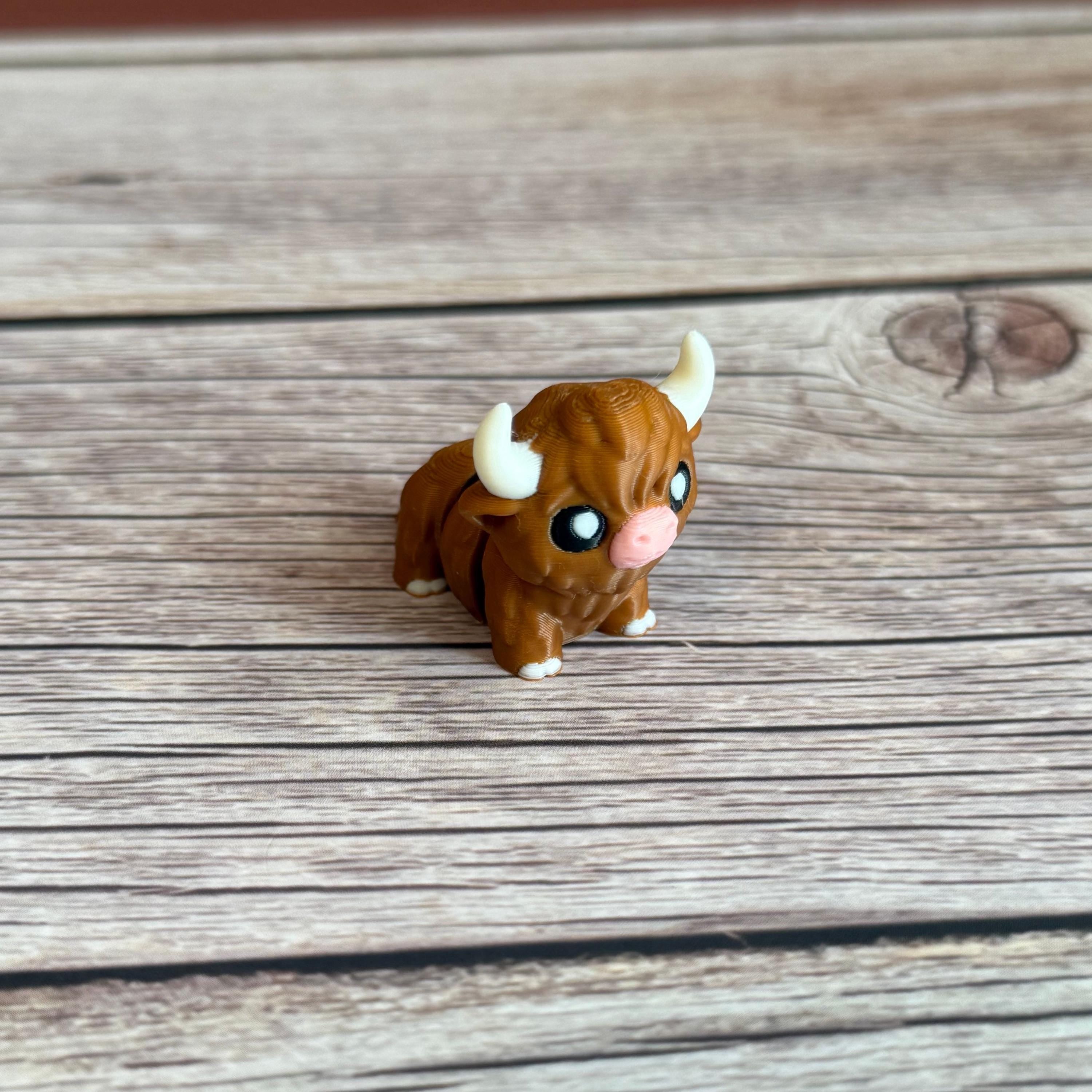 A small 3D printed articulated brown Highland cow toy with movable joints, placed on a wooden surface.