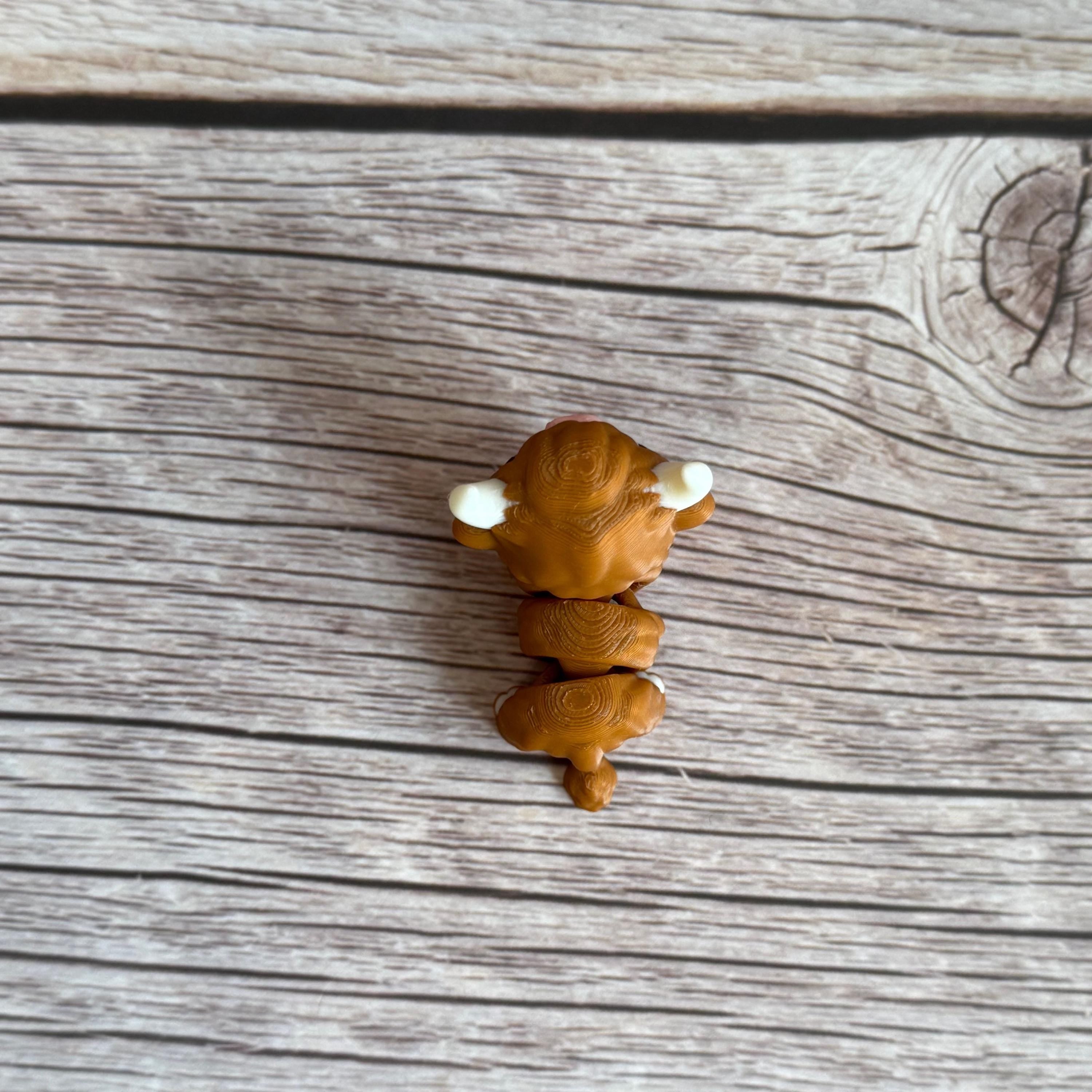 A small 3D printed articulated brown Highland cow toy with movable joints, placed on a wooden surface.
