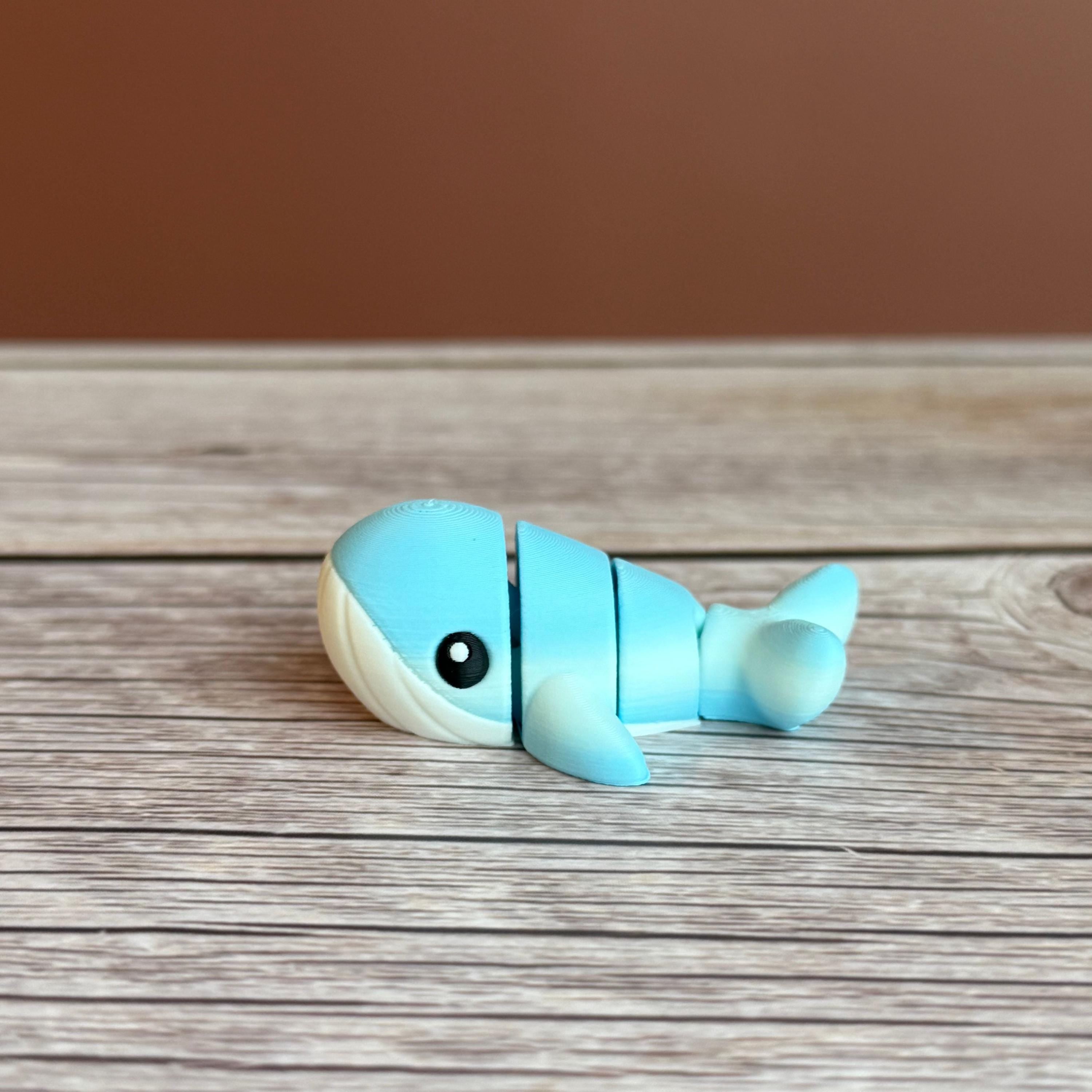 A small 3D printed articulated mini blue and white whale toy with articulated segments placed on a wooden surface