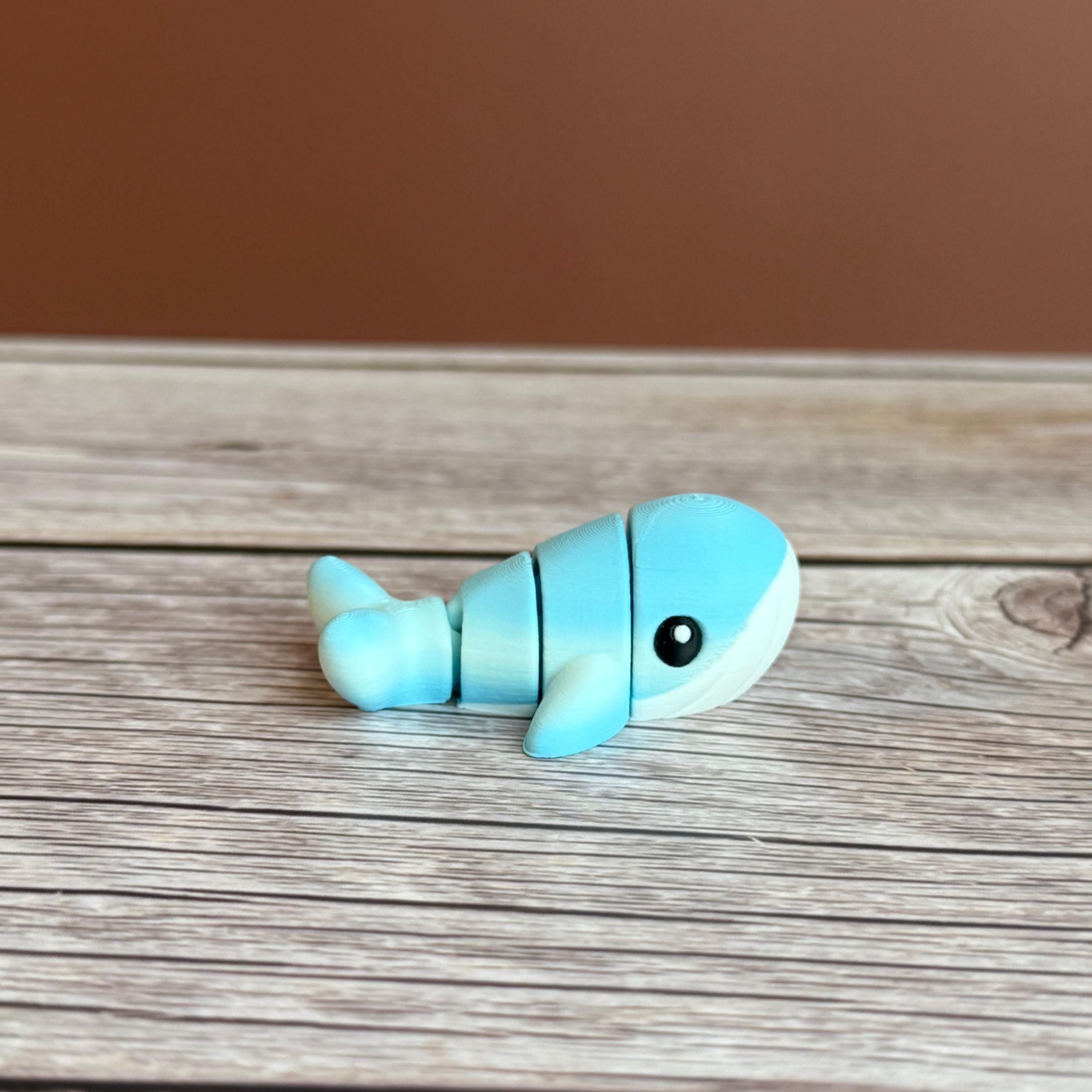 A small 3D printed articulated mini blue and white whale toy with articulated segments placed on a wooden surface