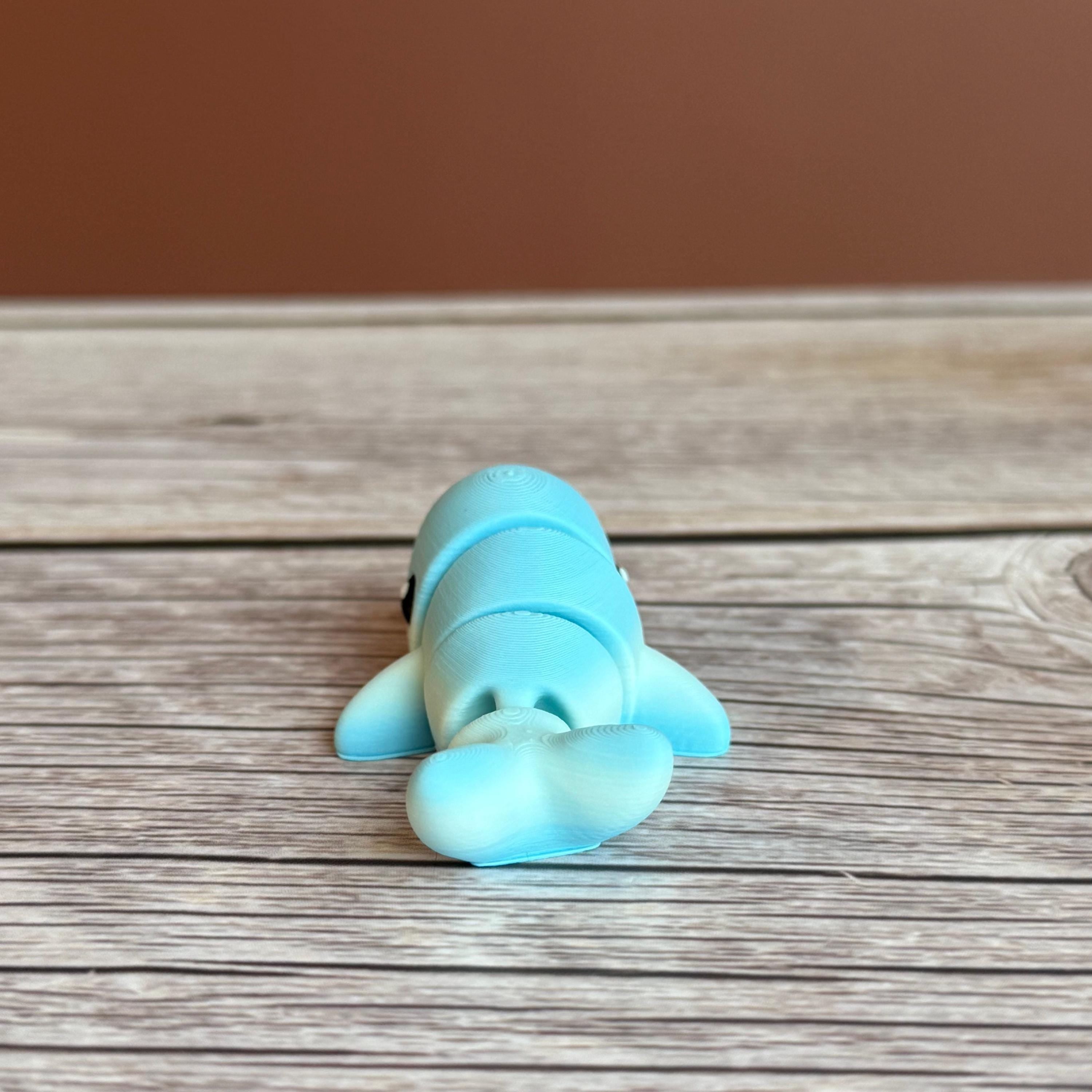 A small 3D printed articulated mini blue and white whale toy with articulated segments placed on a wooden surface