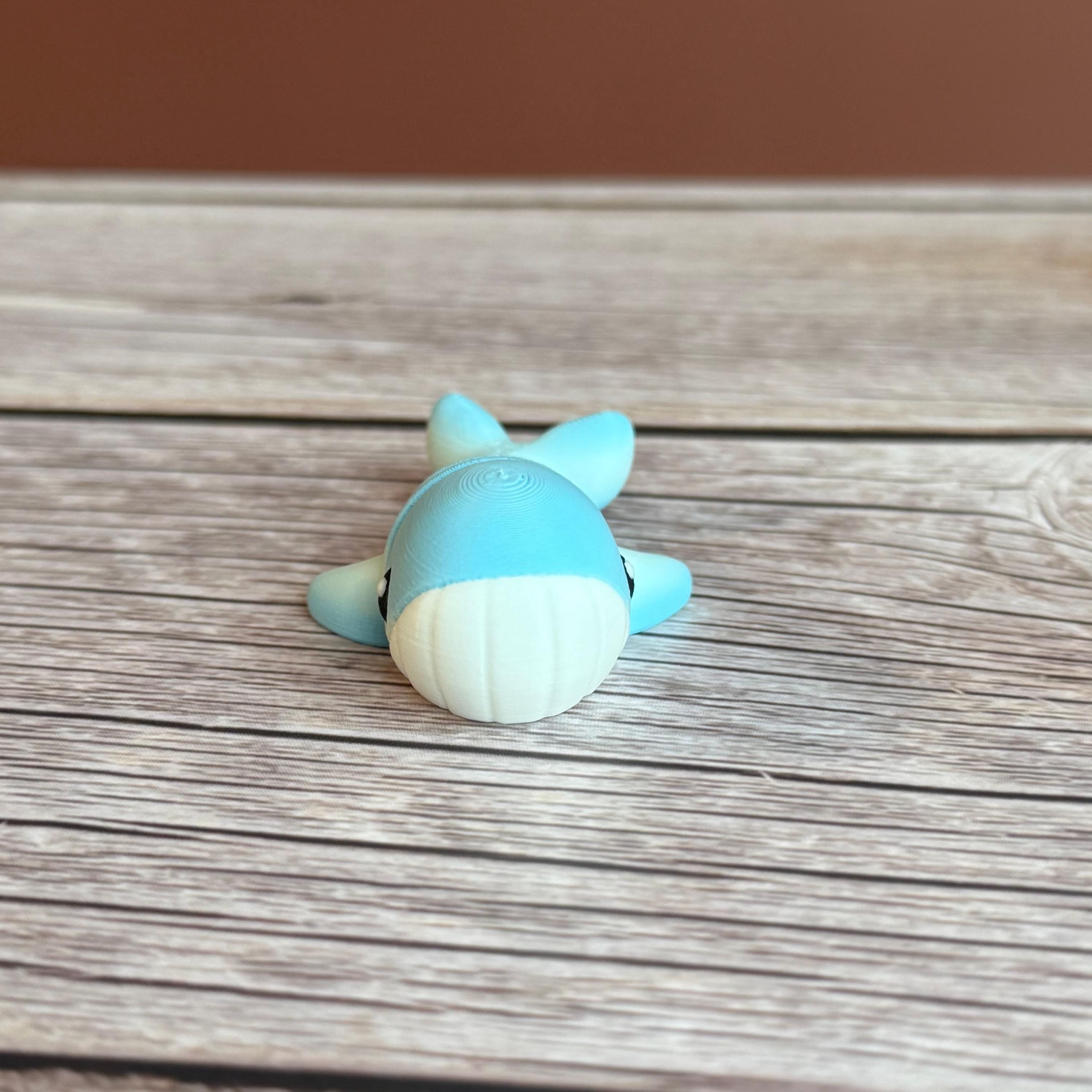 A small 3D printed articulated mini blue and white whale toy with articulated segments placed on a wooden surface
