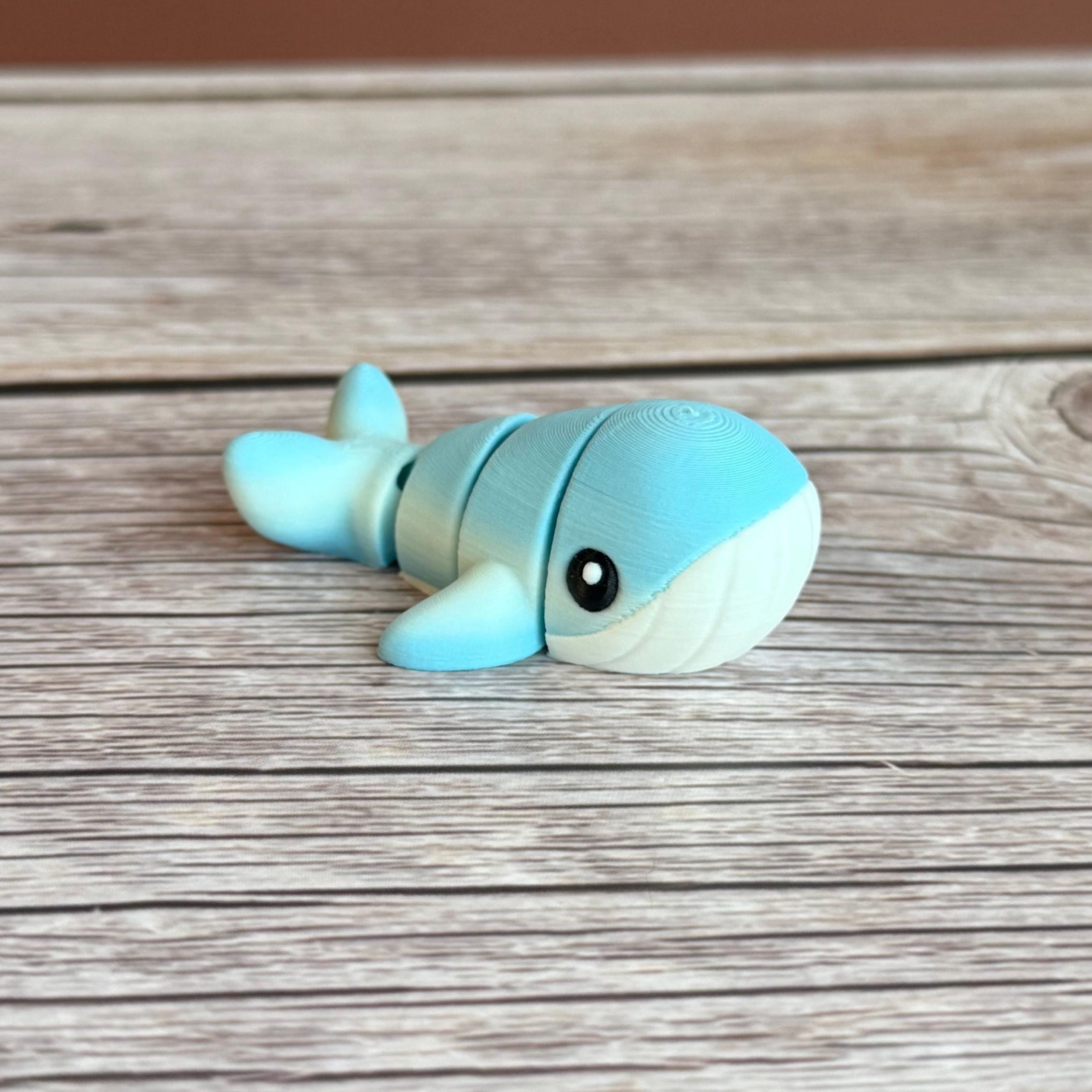A small 3D printed articulated mini blue and white whale toy with articulated segments placed on a wooden surface