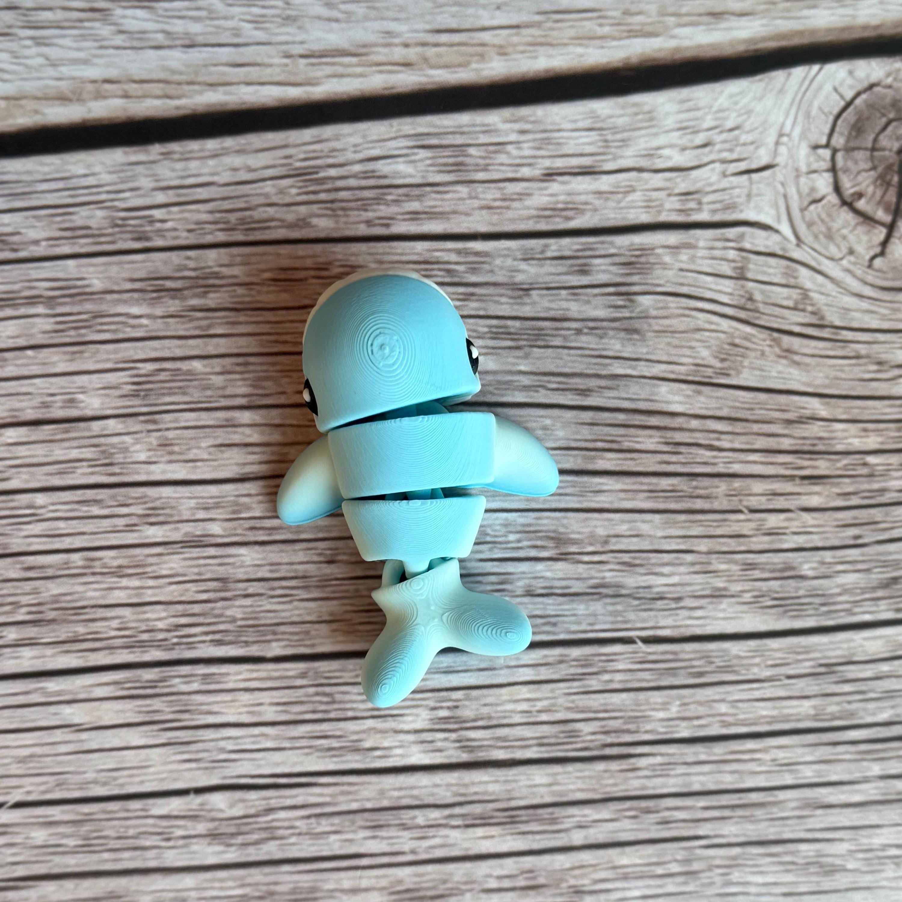 A small 3D printed articulated mini blue and white whale toy with articulated segments placed on a wooden surface