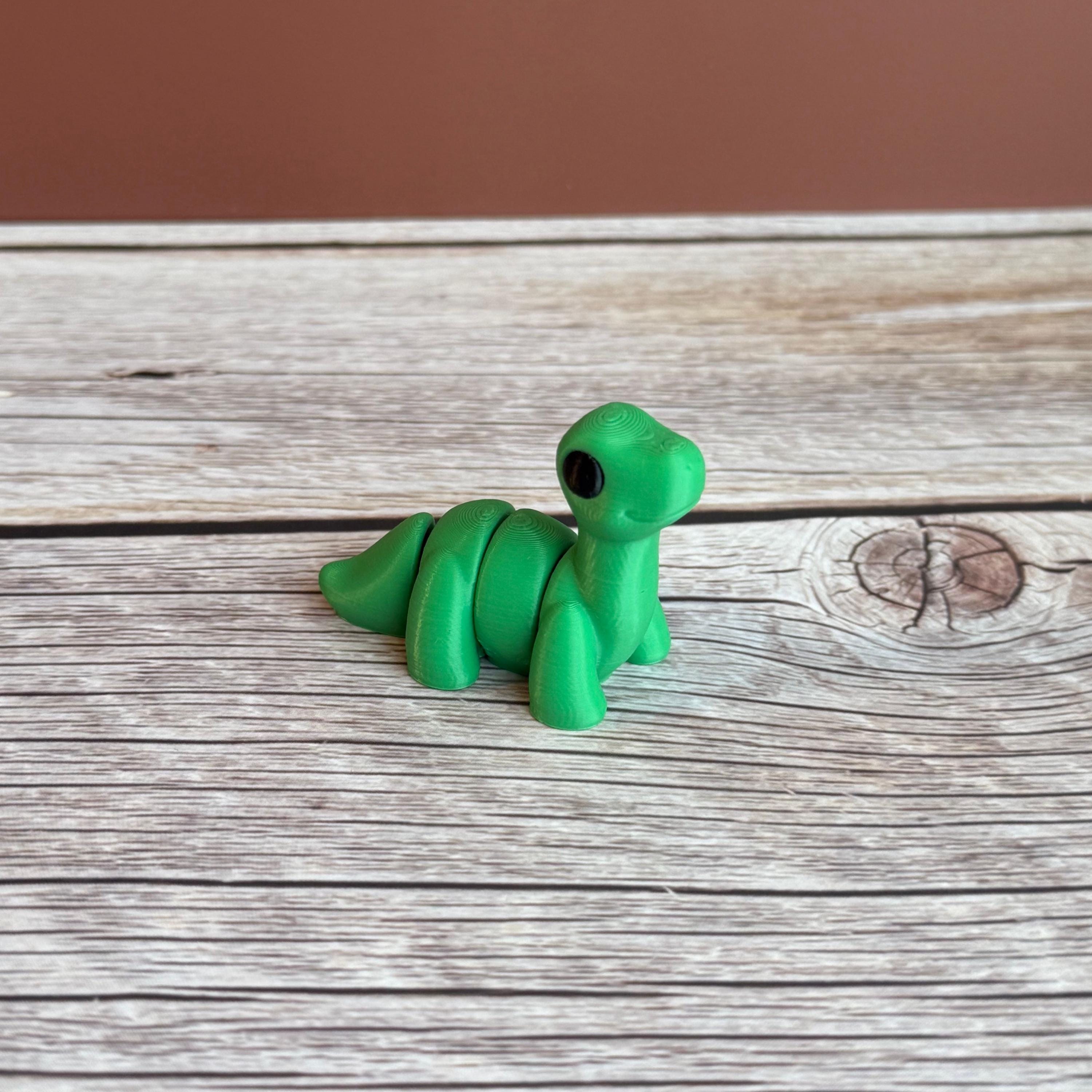 A small green 3D printed articulated Brontosaurus dinosaur toy, sitting on a wooden surface.