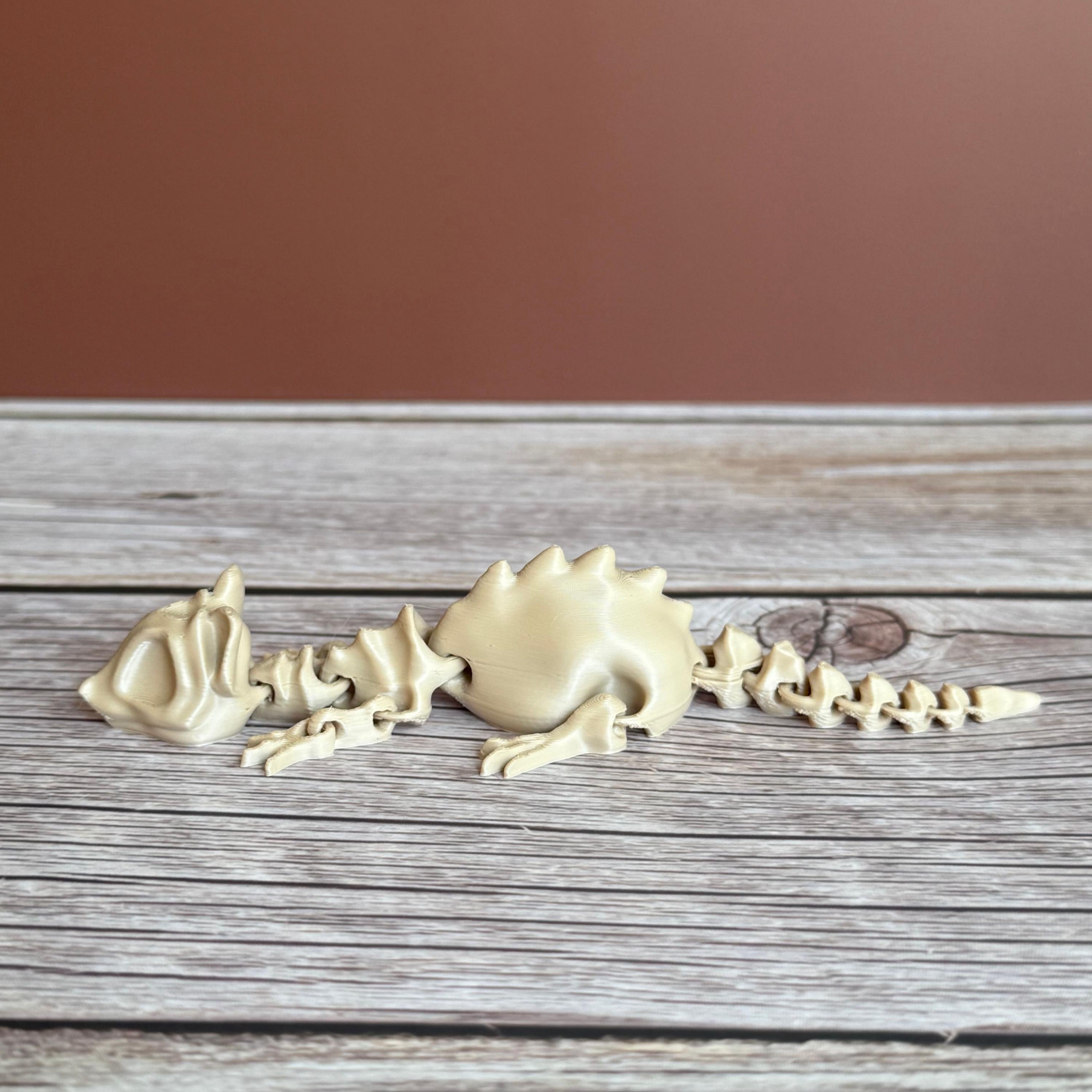 A 3D printed articulated skeleton rat on a wooden surface, with a beige color representing the bone structure.