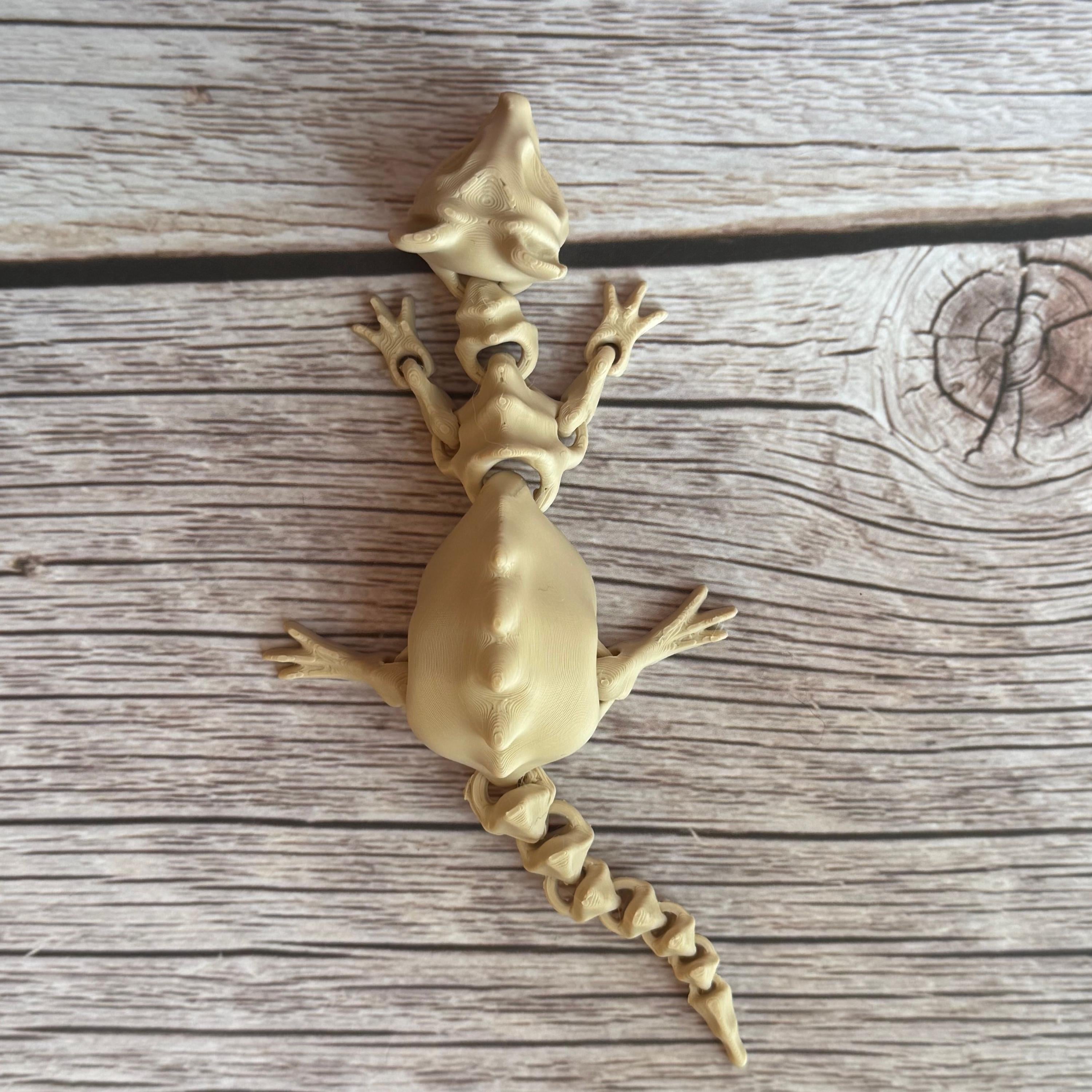 A 3D printed articulated skeleton rat on a wooden surface, with a beige color representing the bone structure.