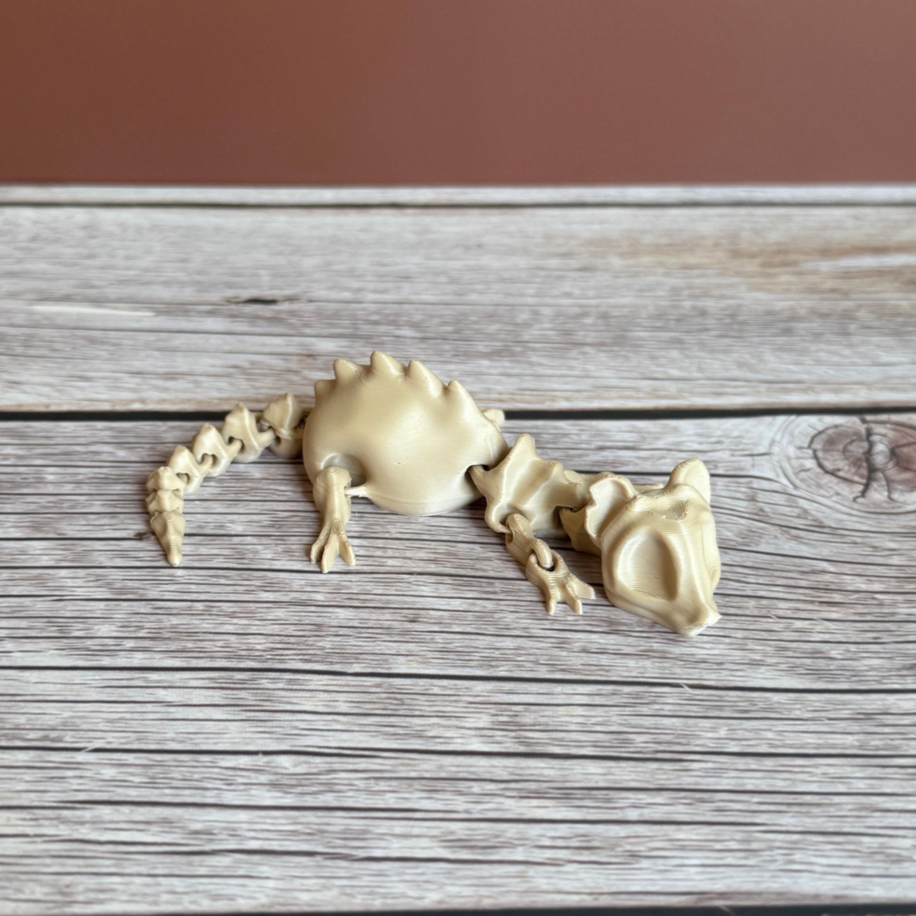 A 3D printed articulated skeleton rat on a wooden surface, with a beige color representing the bone structure.
