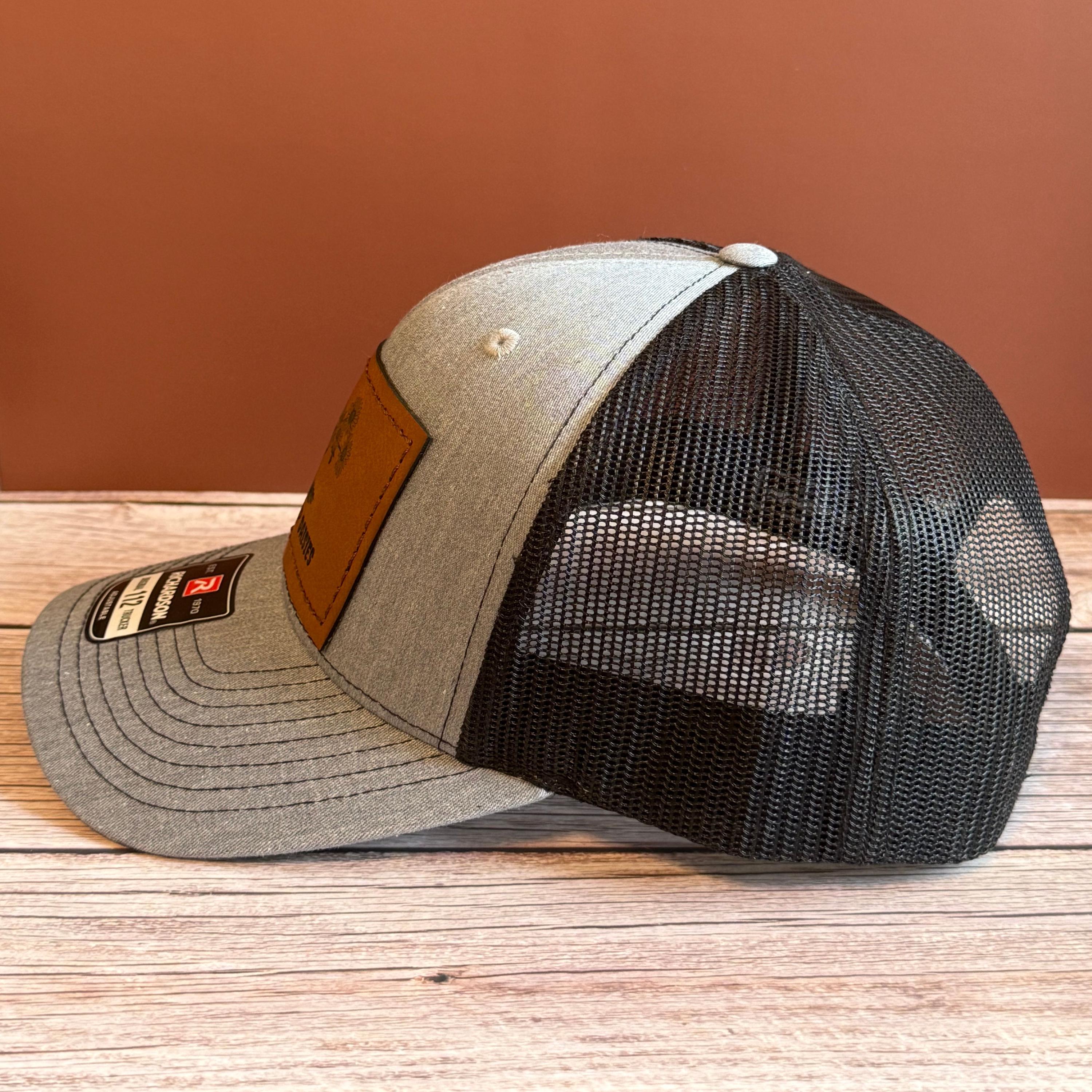 side profile of gray and black snapback hat on a wooden surface against a brown background