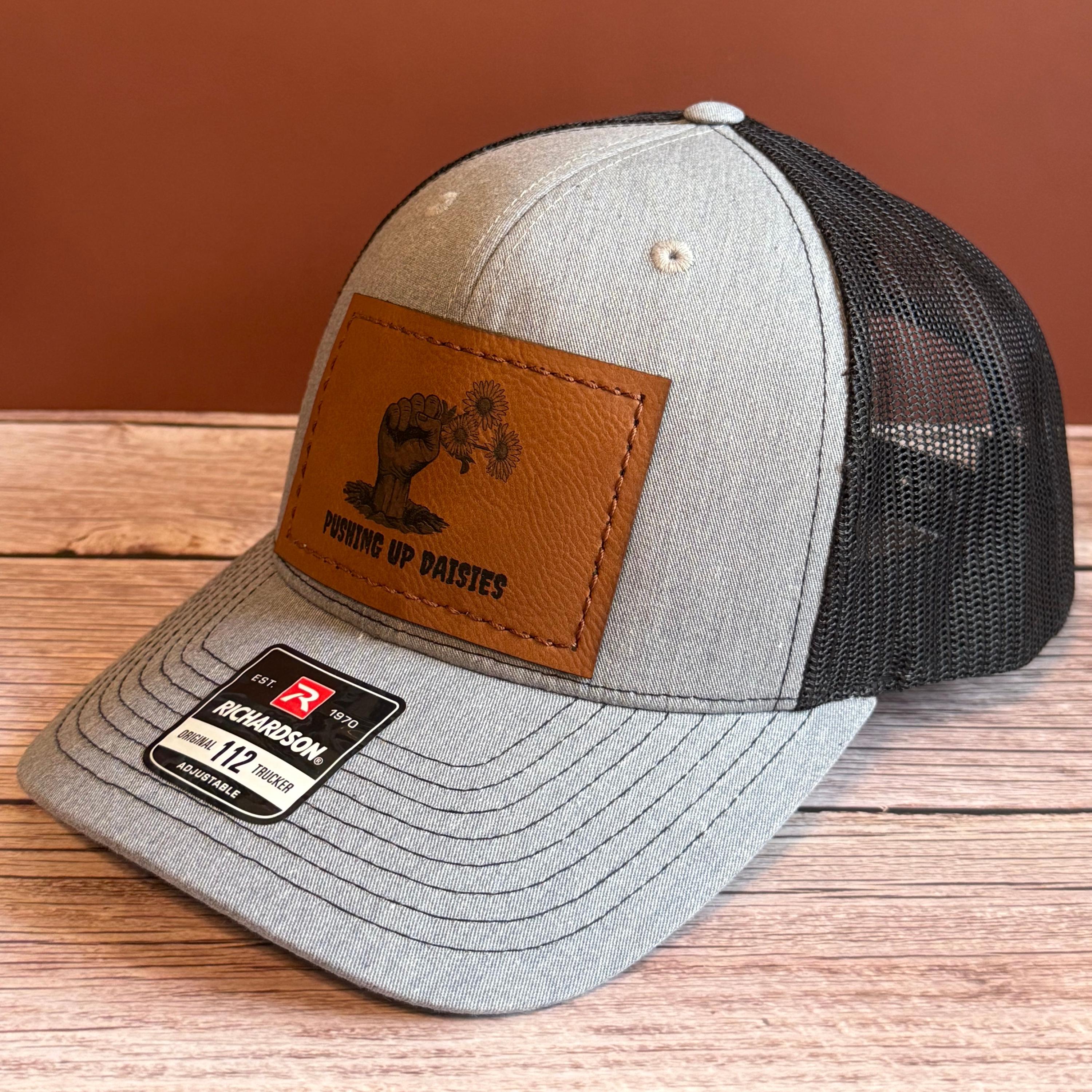 Gray and black snapback hat with rectangular leather patch featuring a zombie hand holding flowers with the phrase 