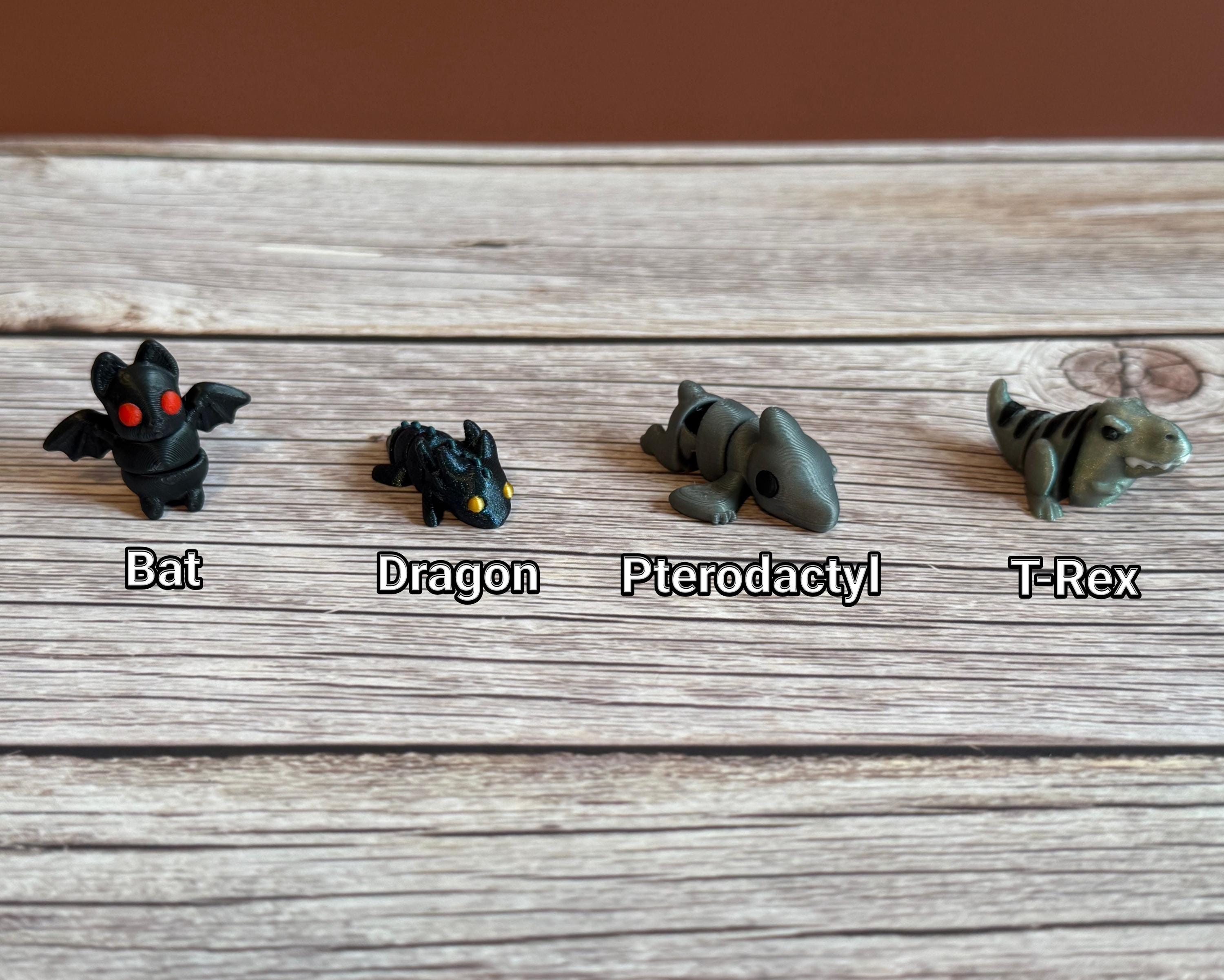 Collection of small animal figurines on a wooden surface. T-rex, pterodactyl, dragon, and bat are featured. 