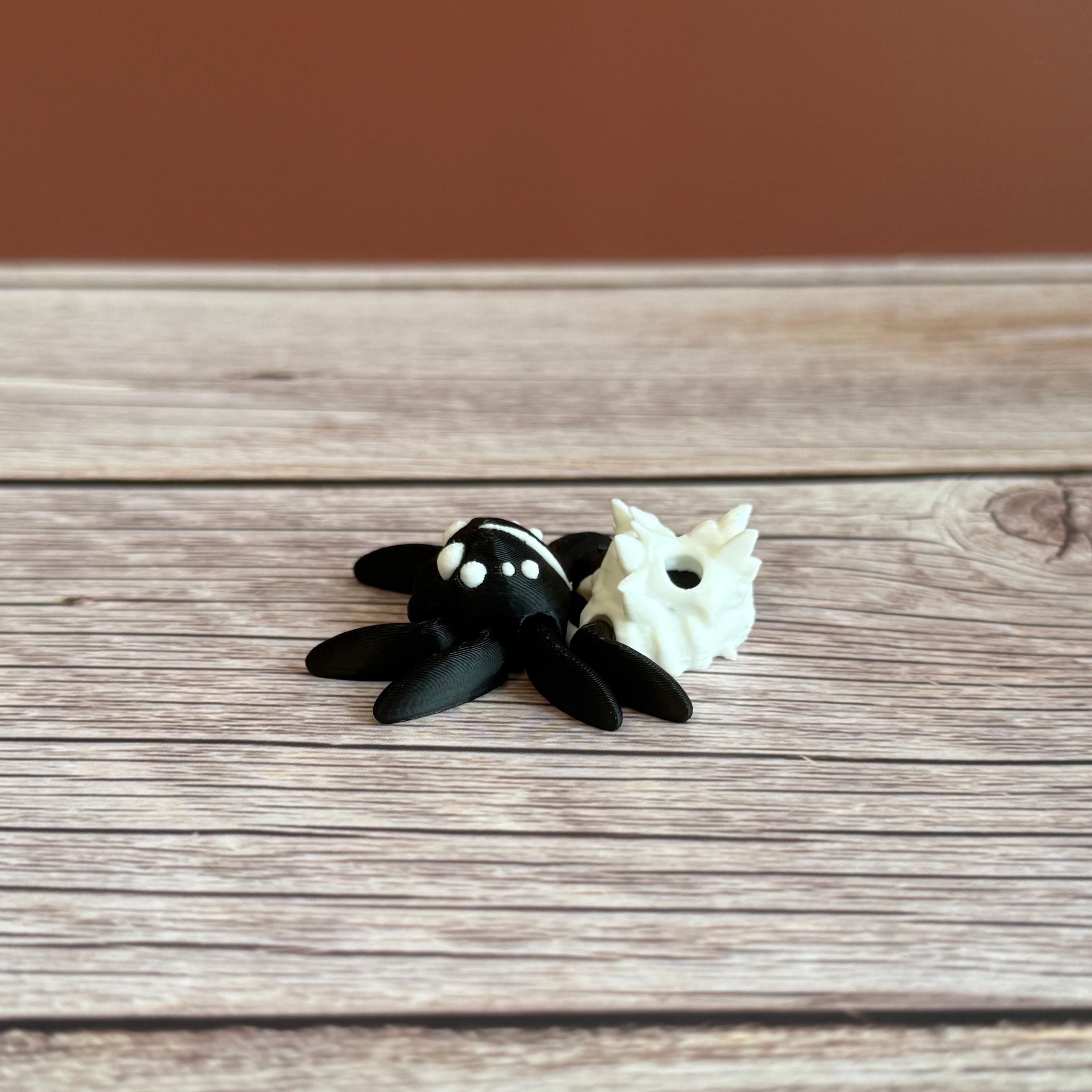 Black and white 3d printed spider featuring a skull on the backside, placed on a wooden surface against a brown backdrop