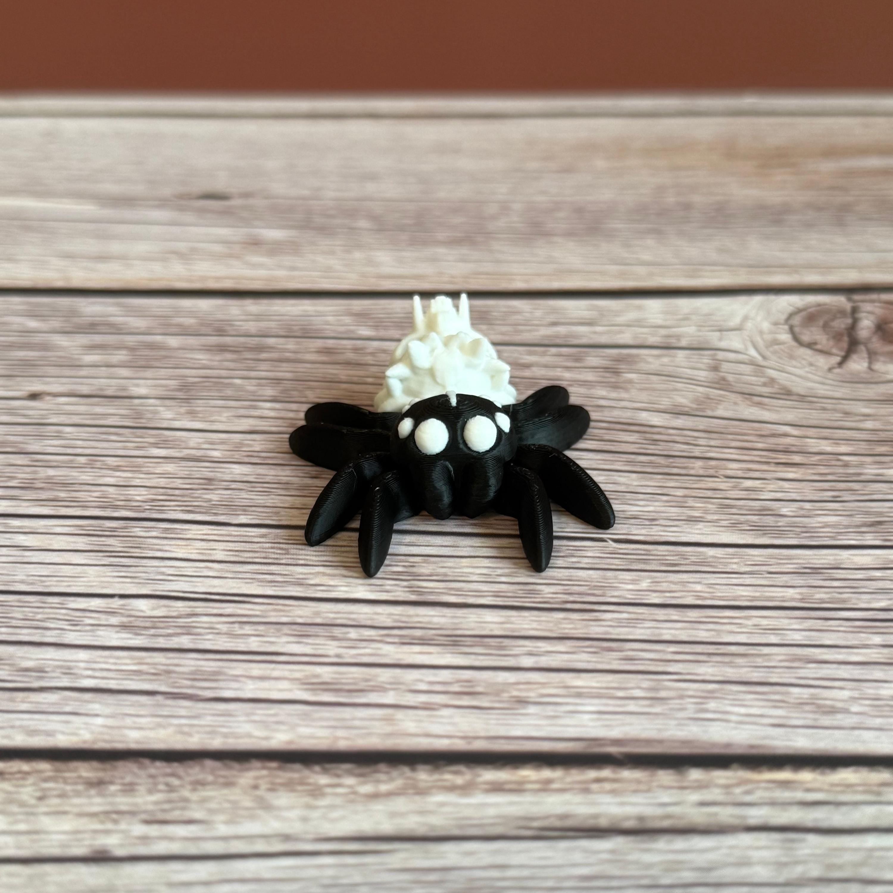 Black and white 3d printed spider featuring a skull on the backside, placed on a wooden surface against a brown backdrop