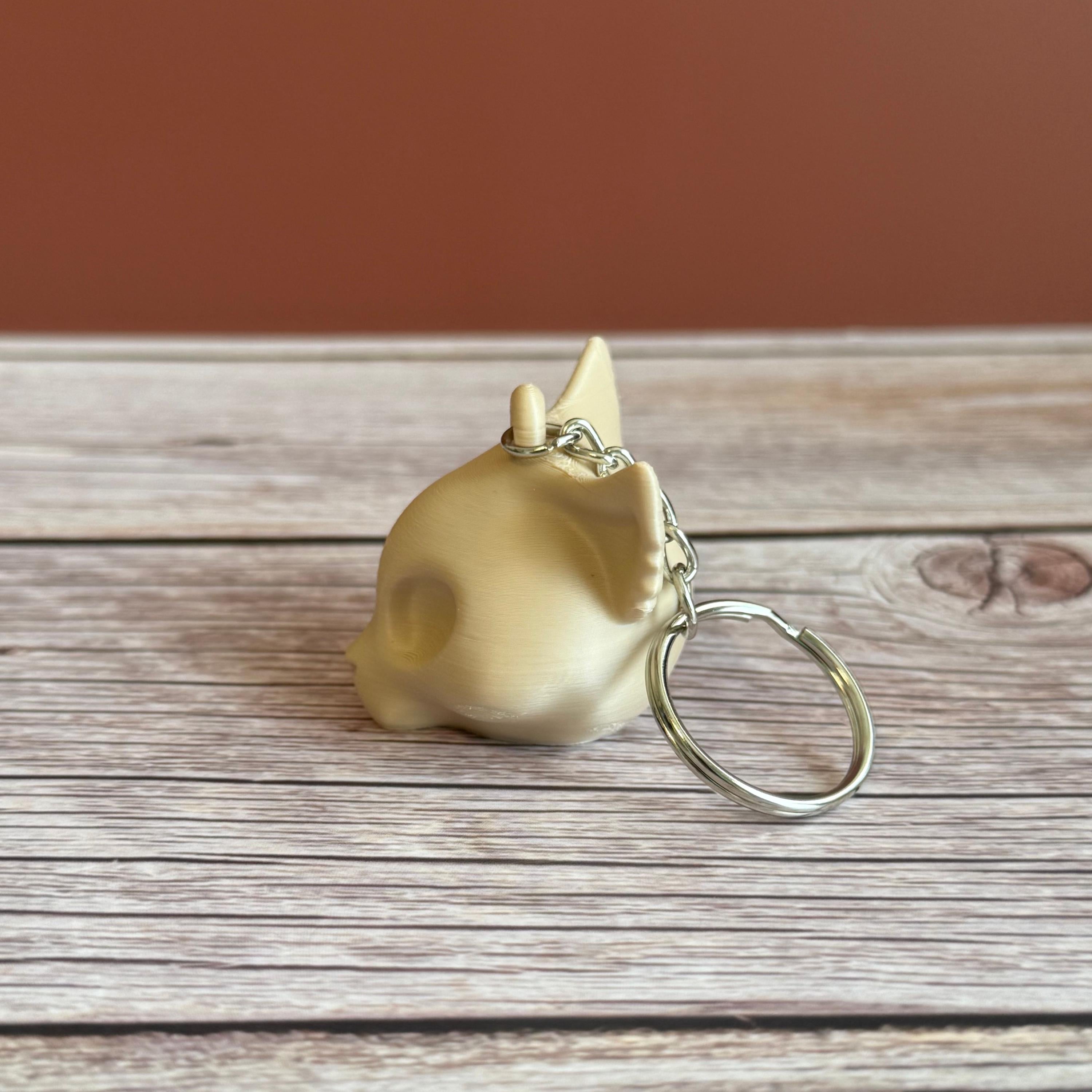 A 3D printed beige cat skull keychain on a wooden surface and brown backdrop