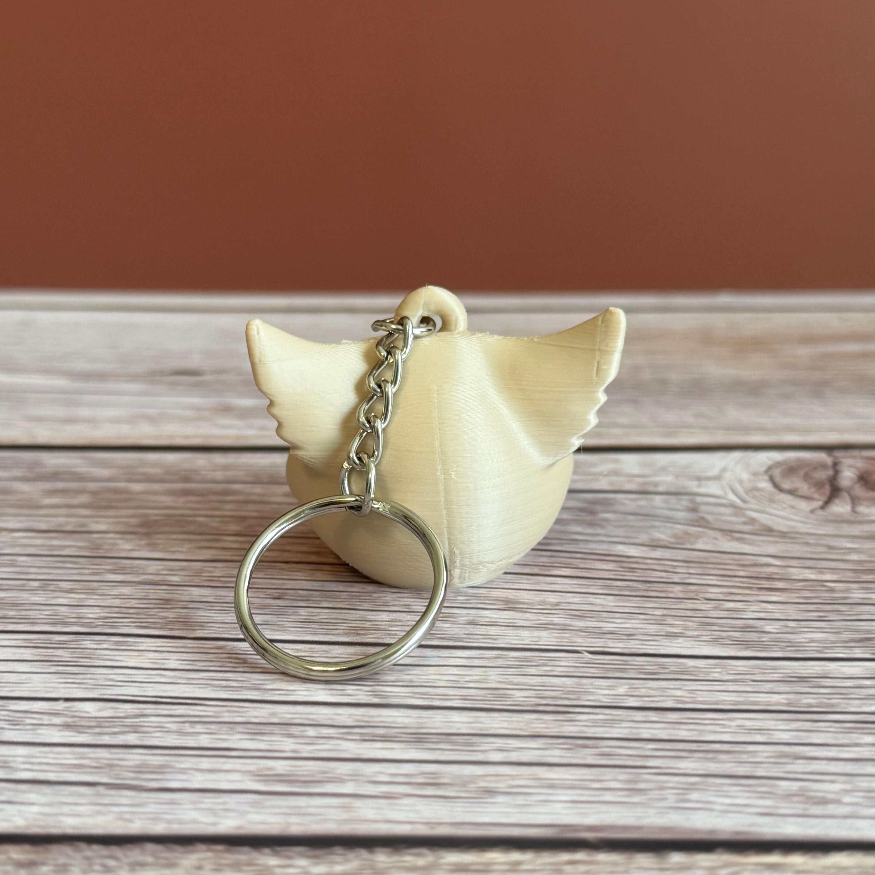 A 3D printed beige cat skull keychain on a wooden surface and brown backdrop