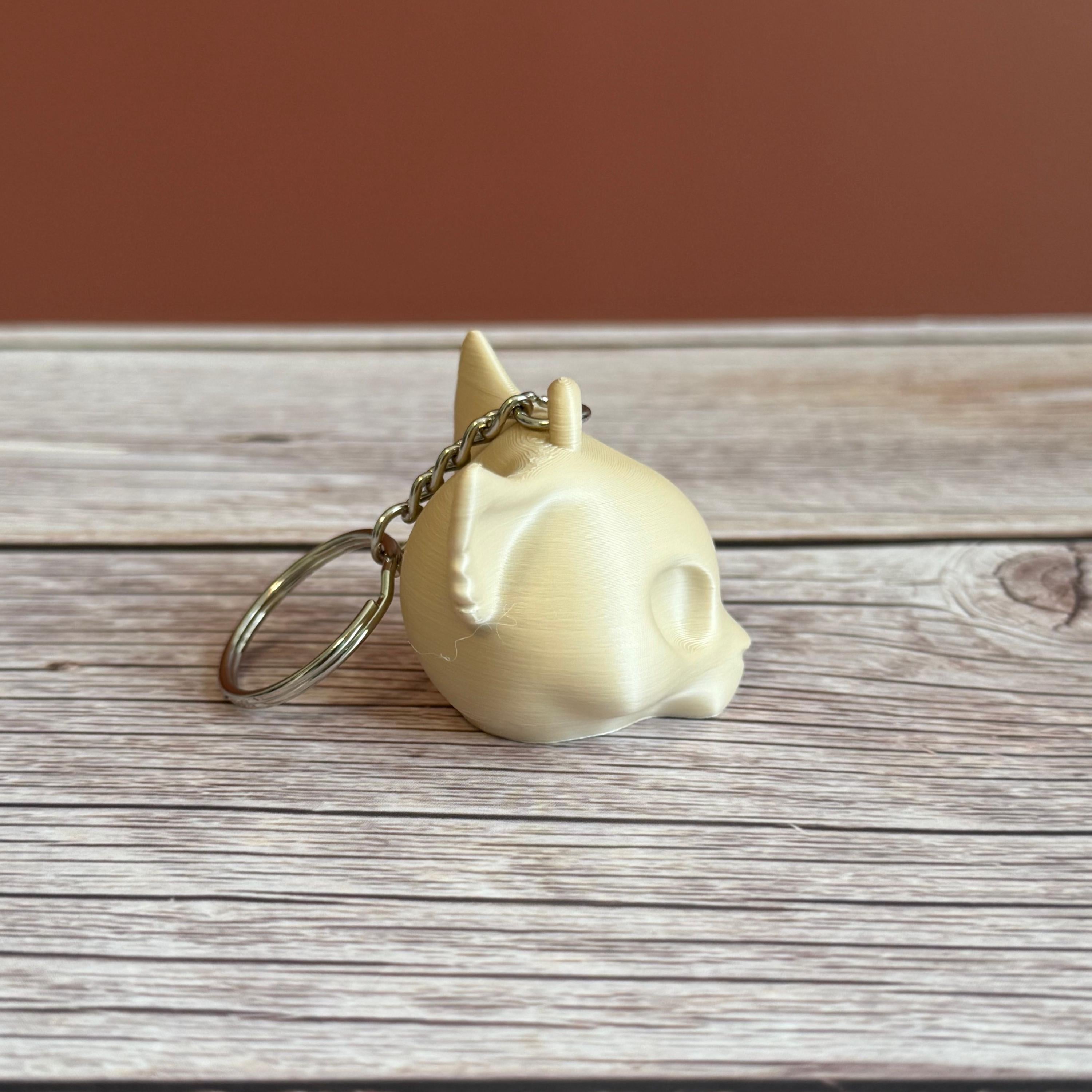 A 3D printed beige cat skull keychain on a wooden surface and brown backdrop