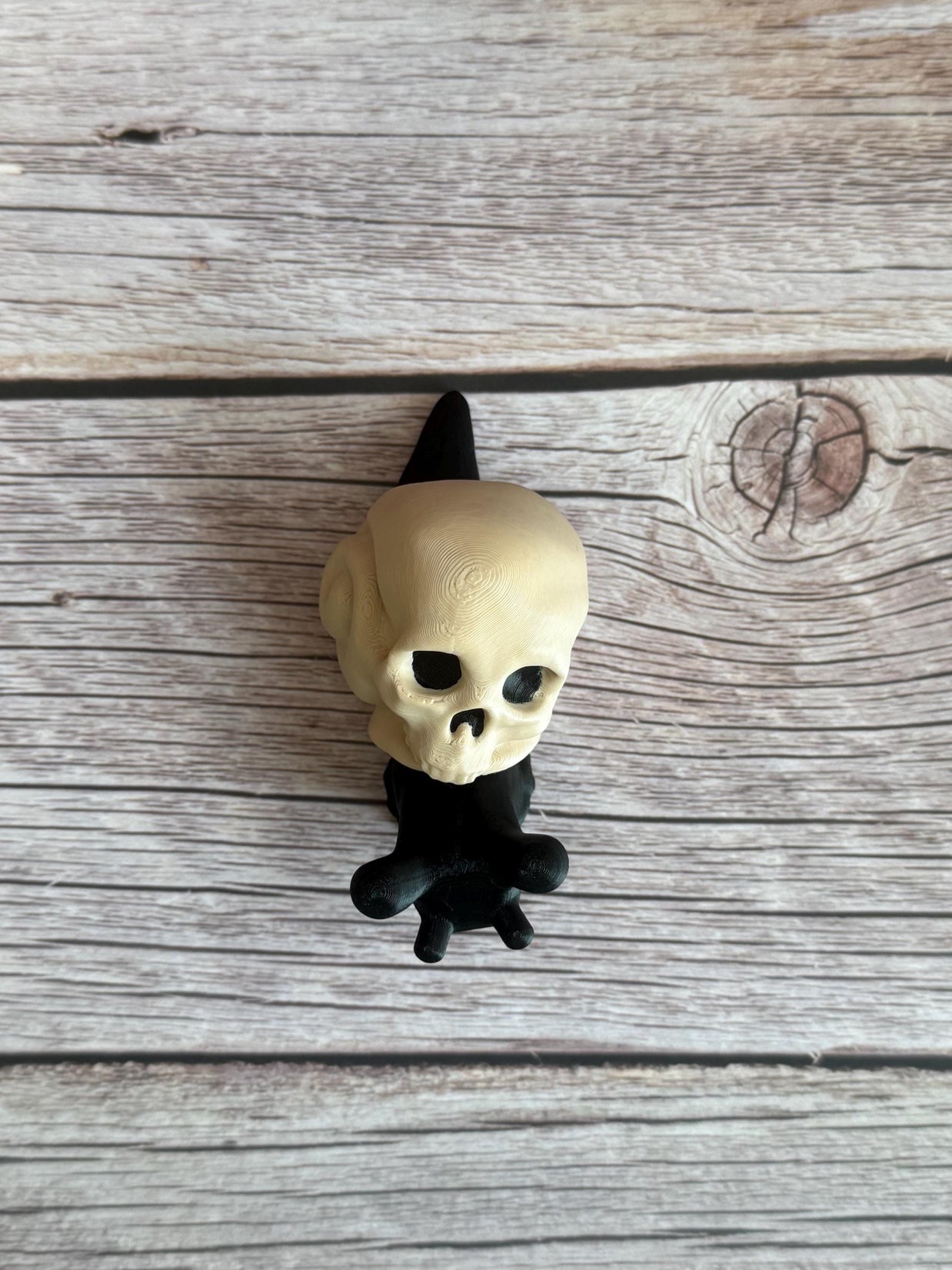 Black 3D printed articulated snail with a beige shell shaped like a human skull, placed on a wooden surface