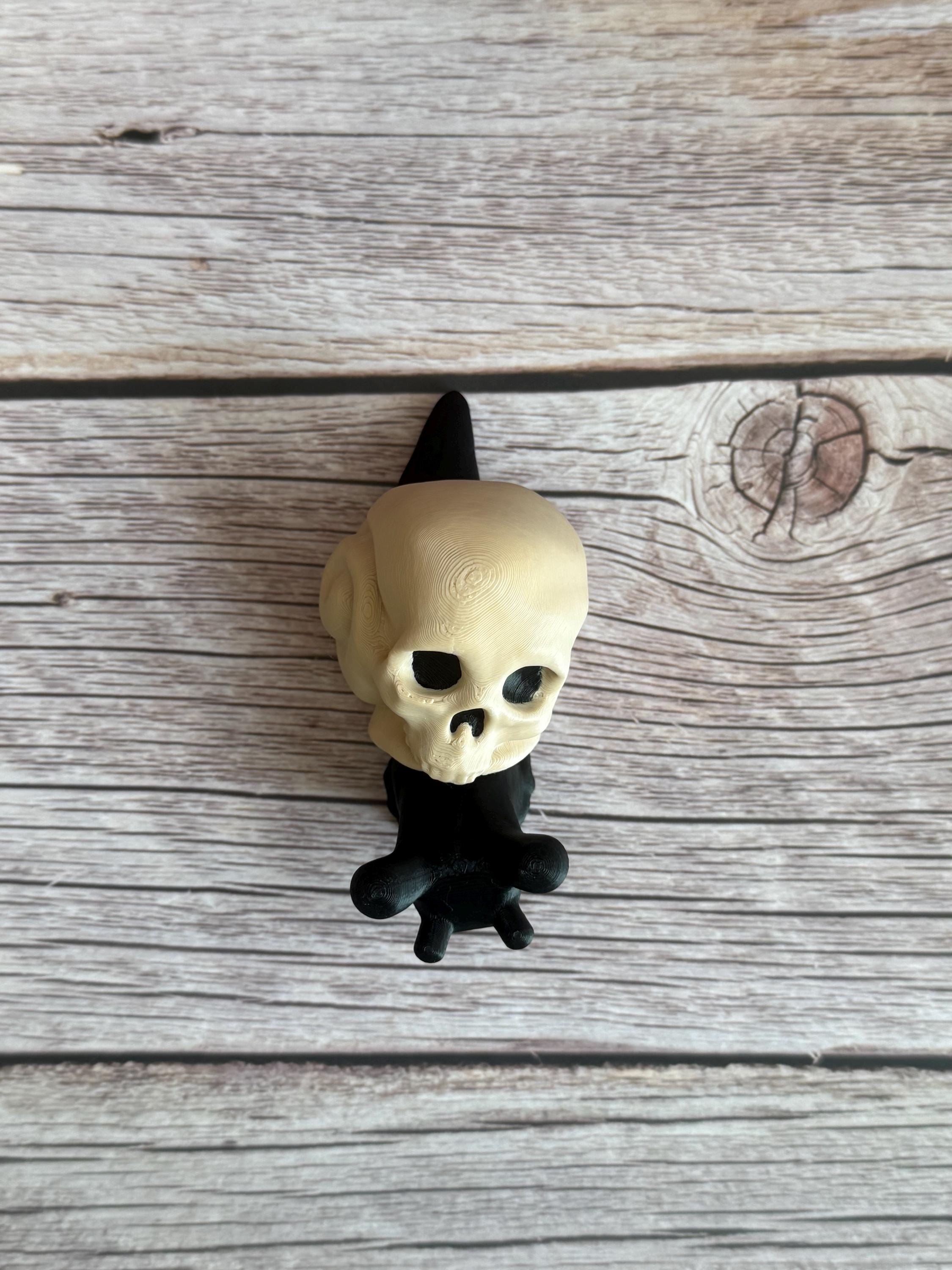 Black 3D printed articulated snail with a beige shell shaped like a human skull, placed on a wooden surface