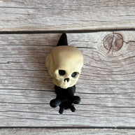 Black 3D printed articulated snail with a beige shell shaped like a human skull, placed on a wooden surface