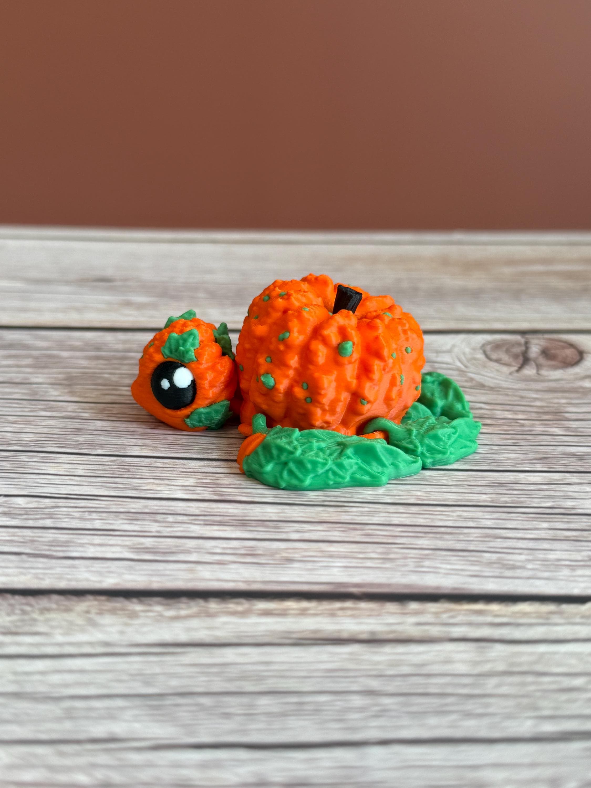 3D printed pumpkin-shaped turtle figure with leaf-like flippers, placed on a wooden surface