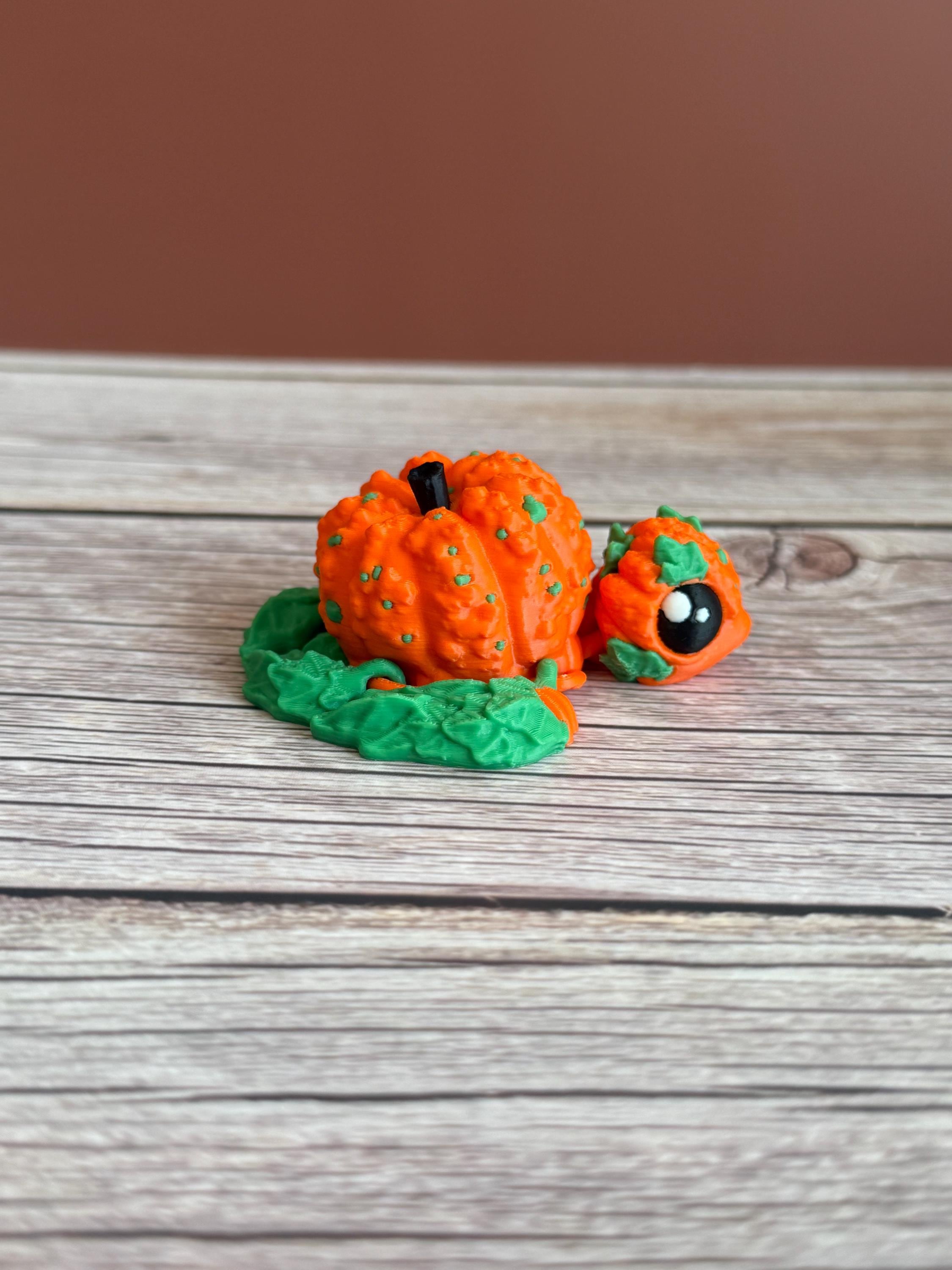 3D printed pumpkin-shaped turtle figure with leaf-like flippers, placed on a wooden surface