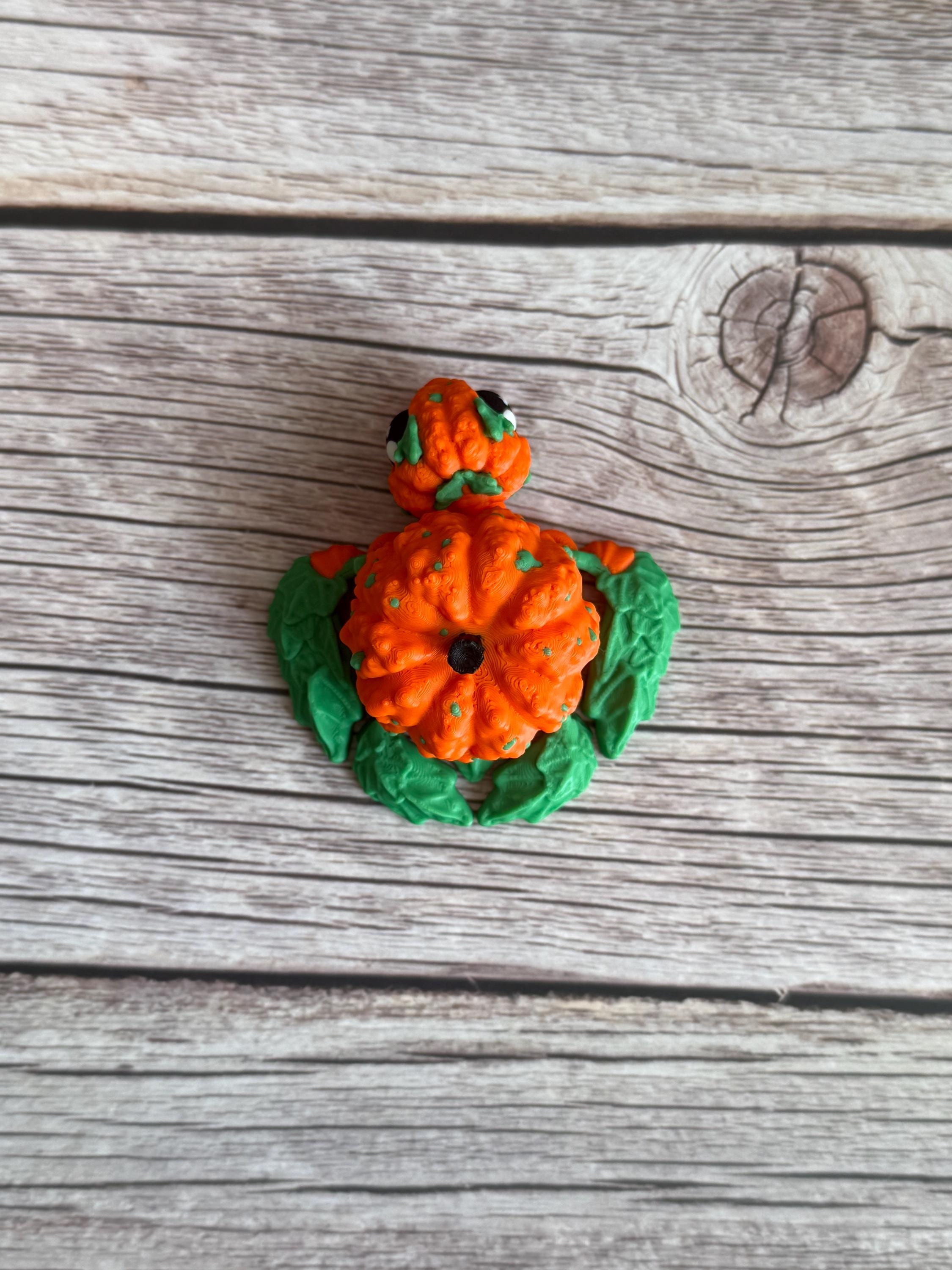 3D printed pumpkin-shaped turtle figure with leaf-like flippers, placed on a wooden surface