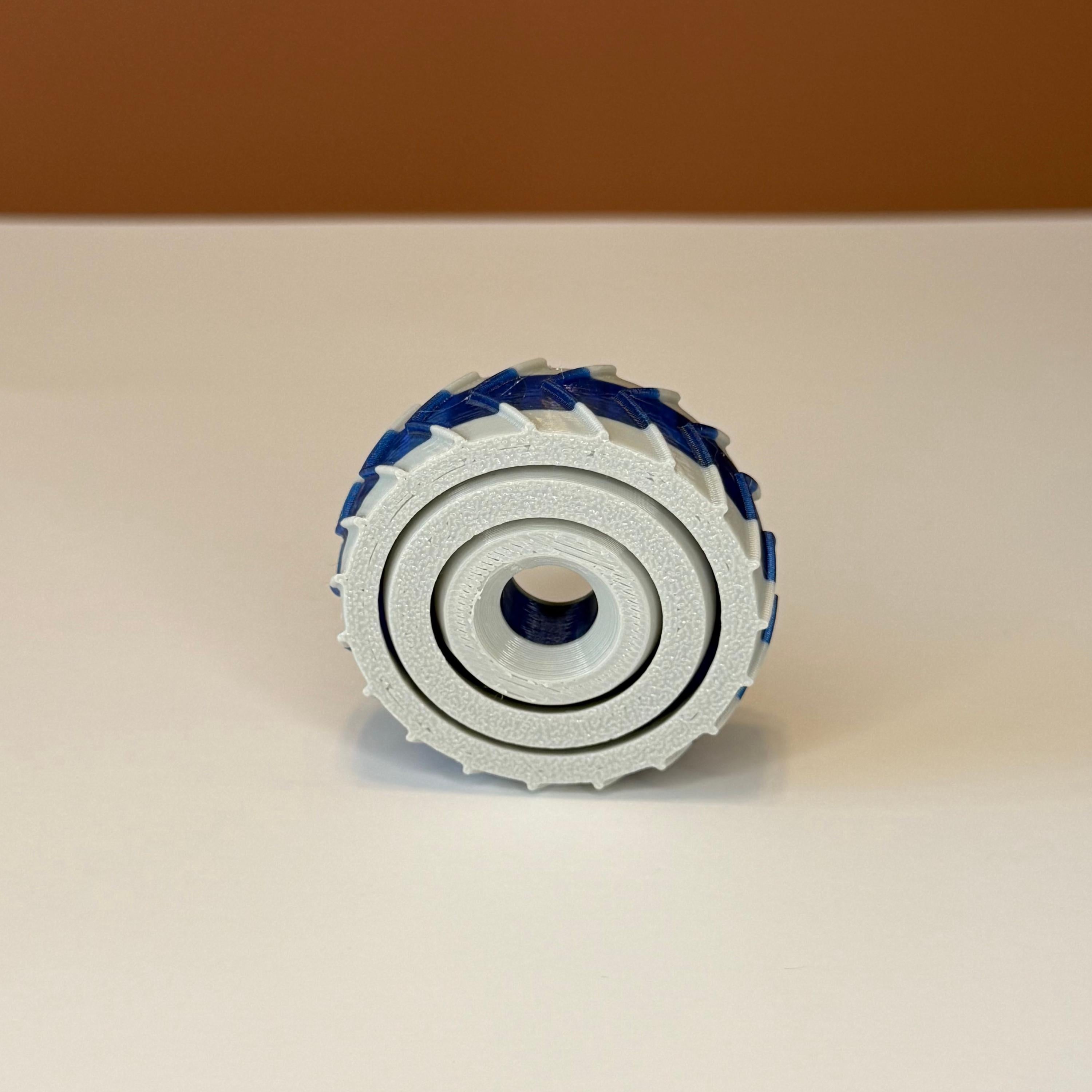 3D printed gray and blue gyro spinner consisting of 3 rings set into each other that spin in different directions on a white and brown background
