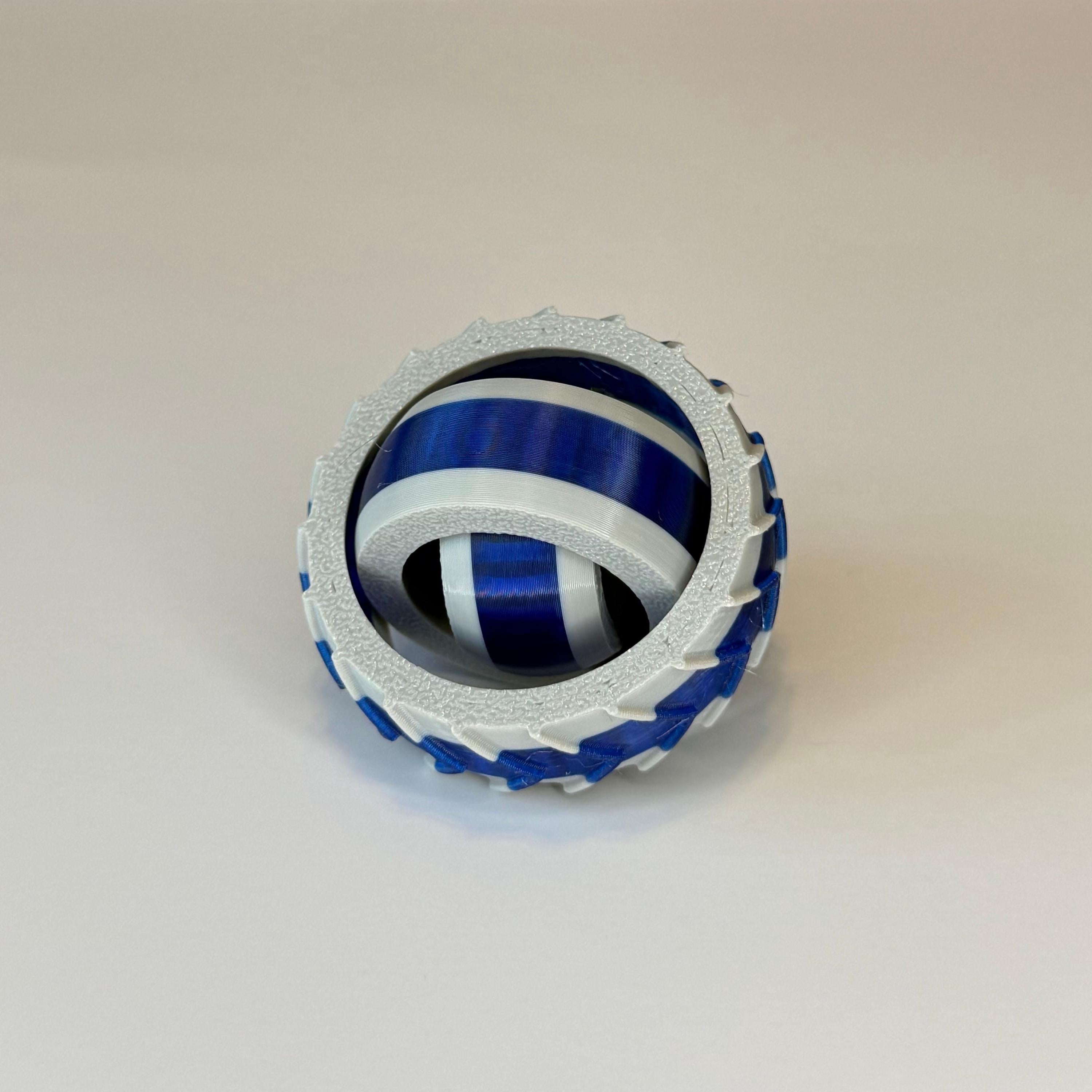3D printed gray and blue gyro spinner consisting of 3 rings set into each other that spin in different directions on a white background