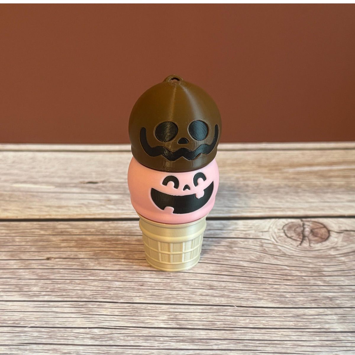 Pink and brown 3D printed ice cream cone keychain with smiling and goofy expressions on the ice cream scoops.