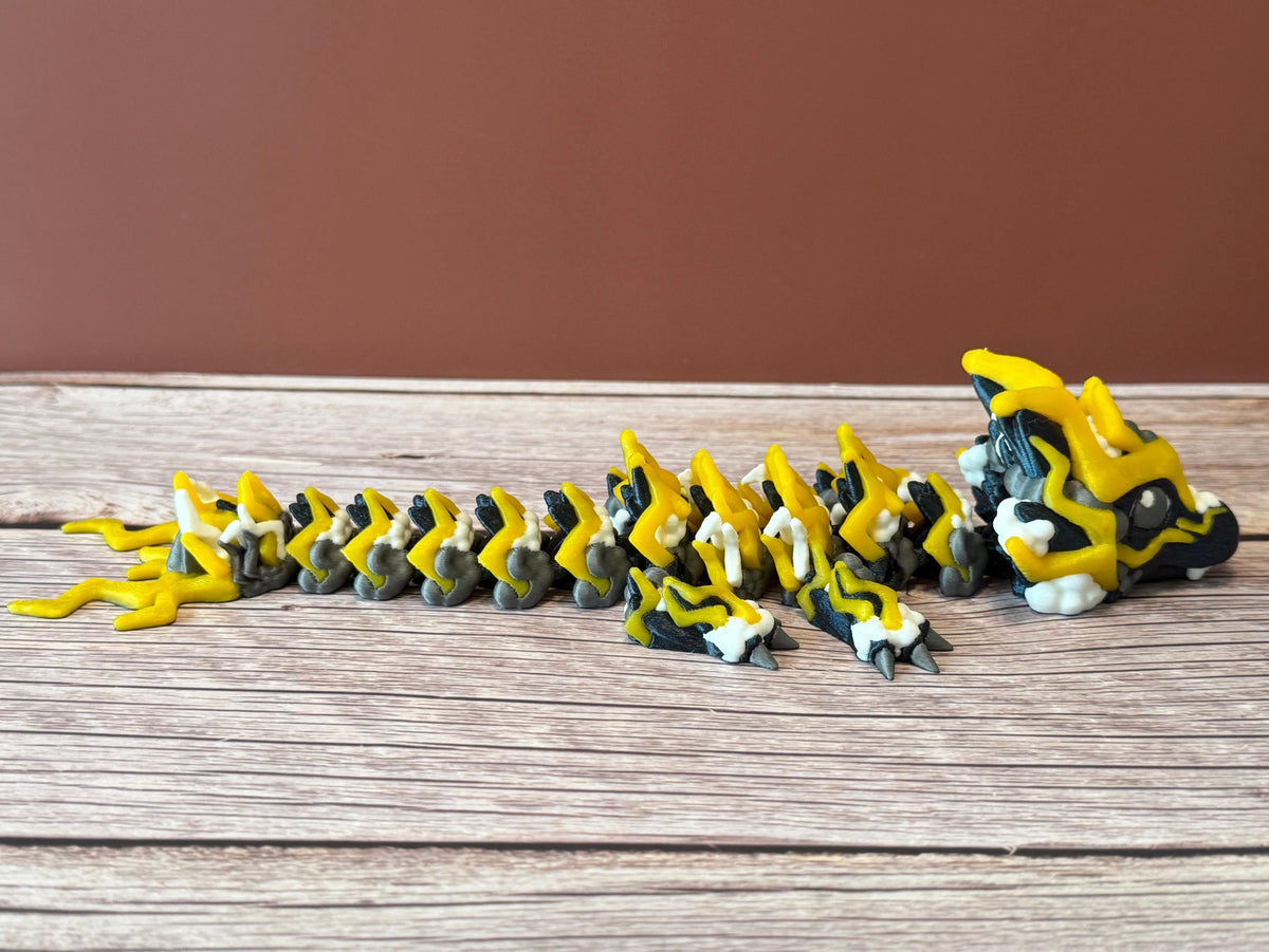 A 3D printed, articulated toy dragon figurine with yellow and black coloring, featuring lightning bolt details and storm cloud patterns, placed on a wooden surface