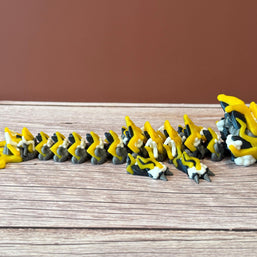 A 3D printed, articulated toy dragon figurine with yellow and black coloring, featuring lightning bolt details and storm cloud patterns, placed on a wooden surface
