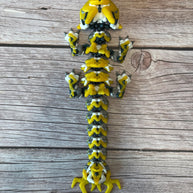 A 3D printed, articulated toy dragon figurine with yellow and black coloring, featuring lightning bolt details and storm cloud patterns, placed on a wooden surface