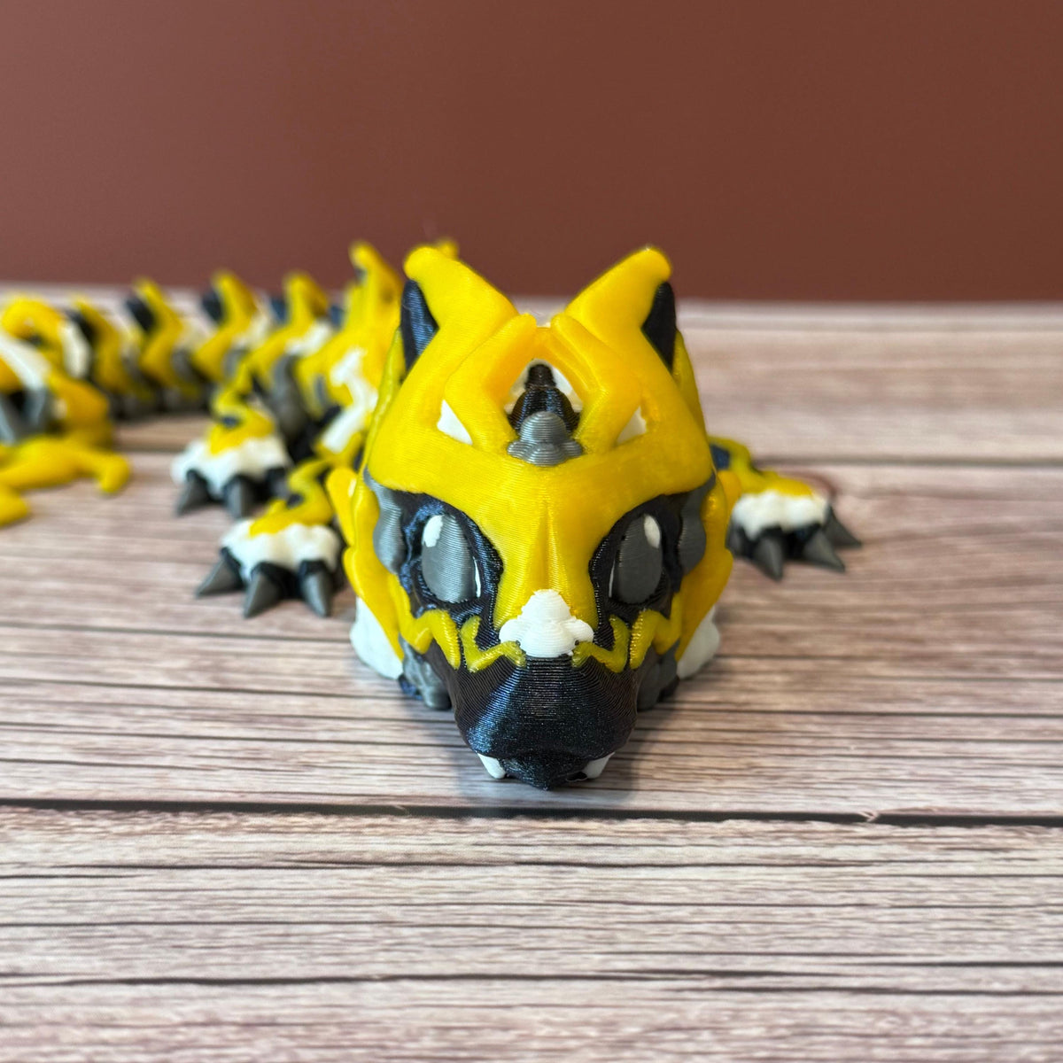 A 3D printed, articulated toy dragon figurine with yellow and black coloring, featuring lightning bolt details and storm cloud patterns, placed on a wooden surface