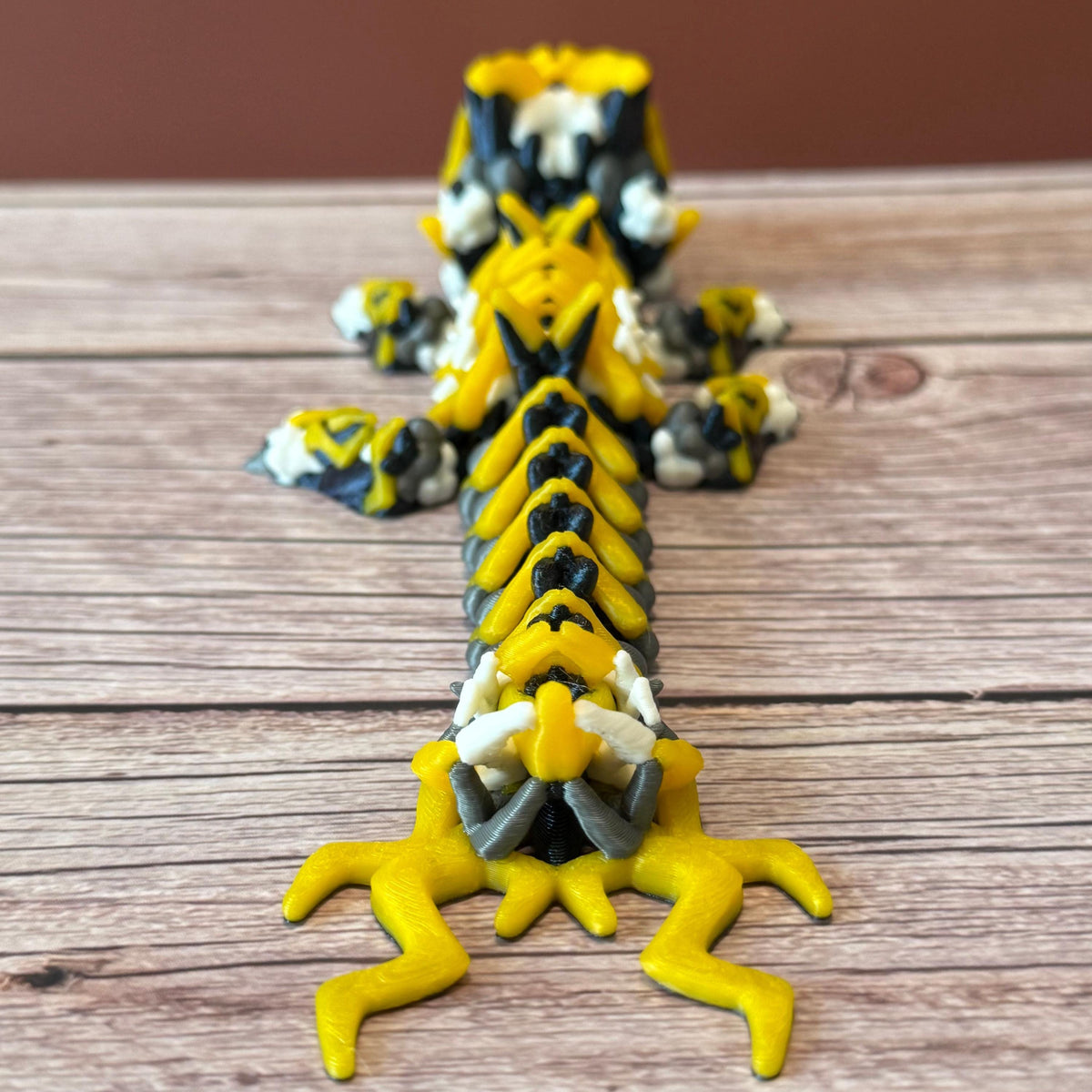 A 3D printed, articulated toy dragon figurine with yellow and black coloring, featuring lightning bolt details and storm cloud patterns, placed on a wooden surface