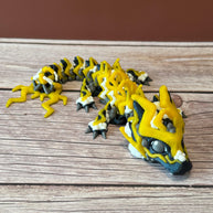 A 3D printed, articulated toy dragon figurine with yellow and black coloring, featuring lightning bolt details and storm cloud patterns, placed on a wooden surface