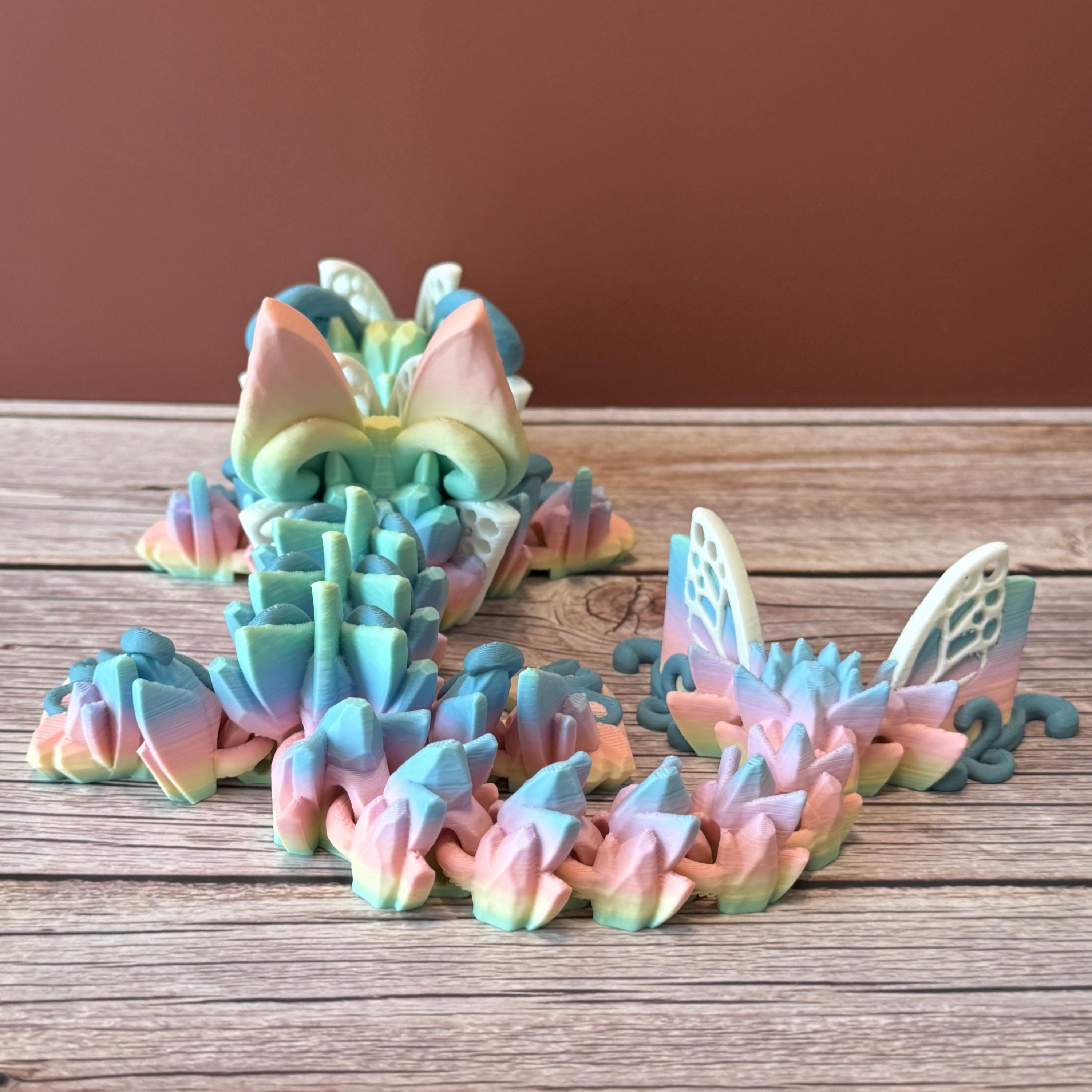 A 3D printed articulated fantasy creature resembling a dragon with butterfly features, in multicolor design, placed on a wooden surface