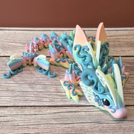 A 3D printed articulated fantasy creature resembling a dragon with butterfly features, in multicolor design, placed on a wooden surface