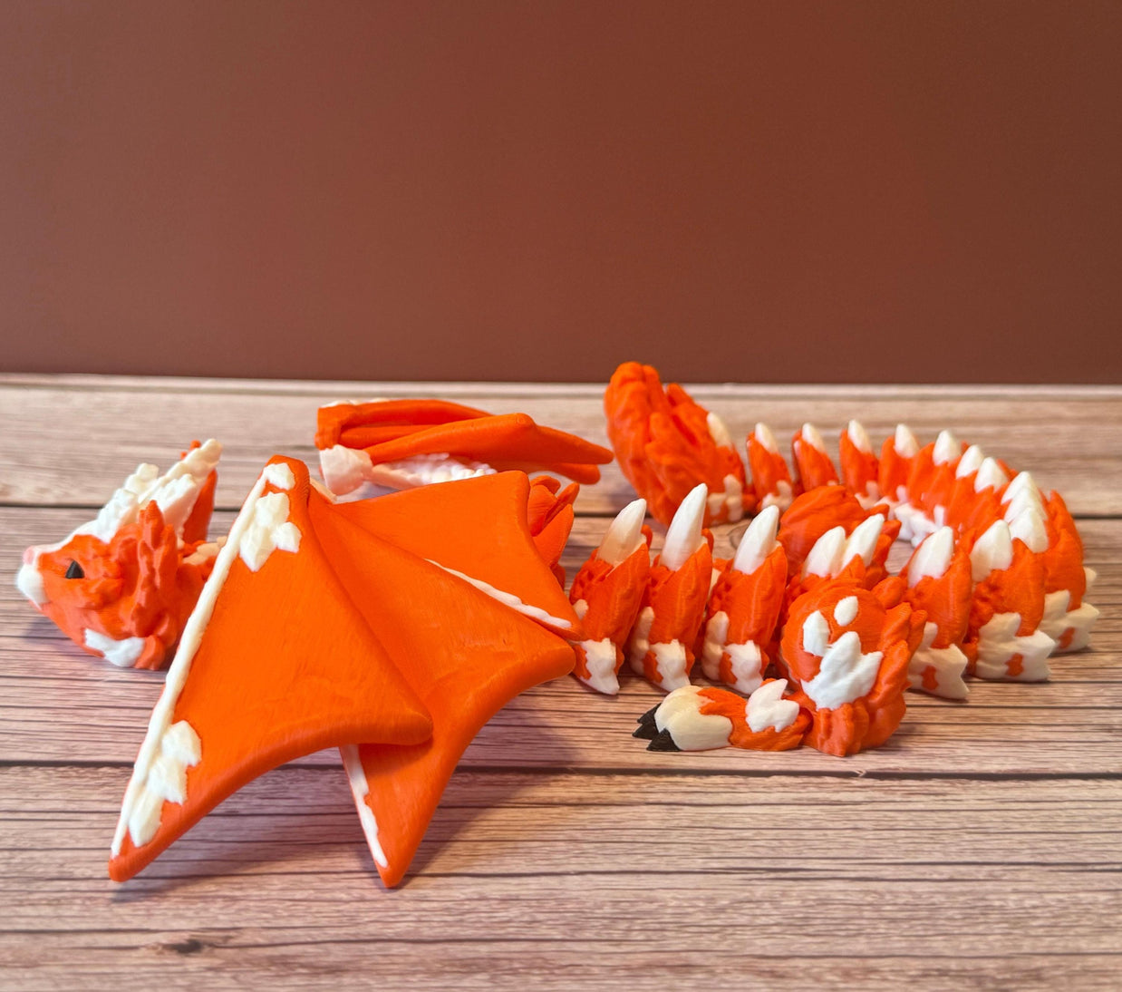 Orange and white 3D printed dragon figurine featuring a hybrid design of a dragon and a cat, placed on a wooden surface